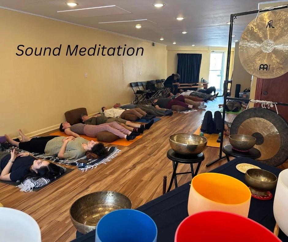Group of people lying on mats on the floor in a meditation session in a room with yellow walls, with sound bowls and a gong in the foreground.