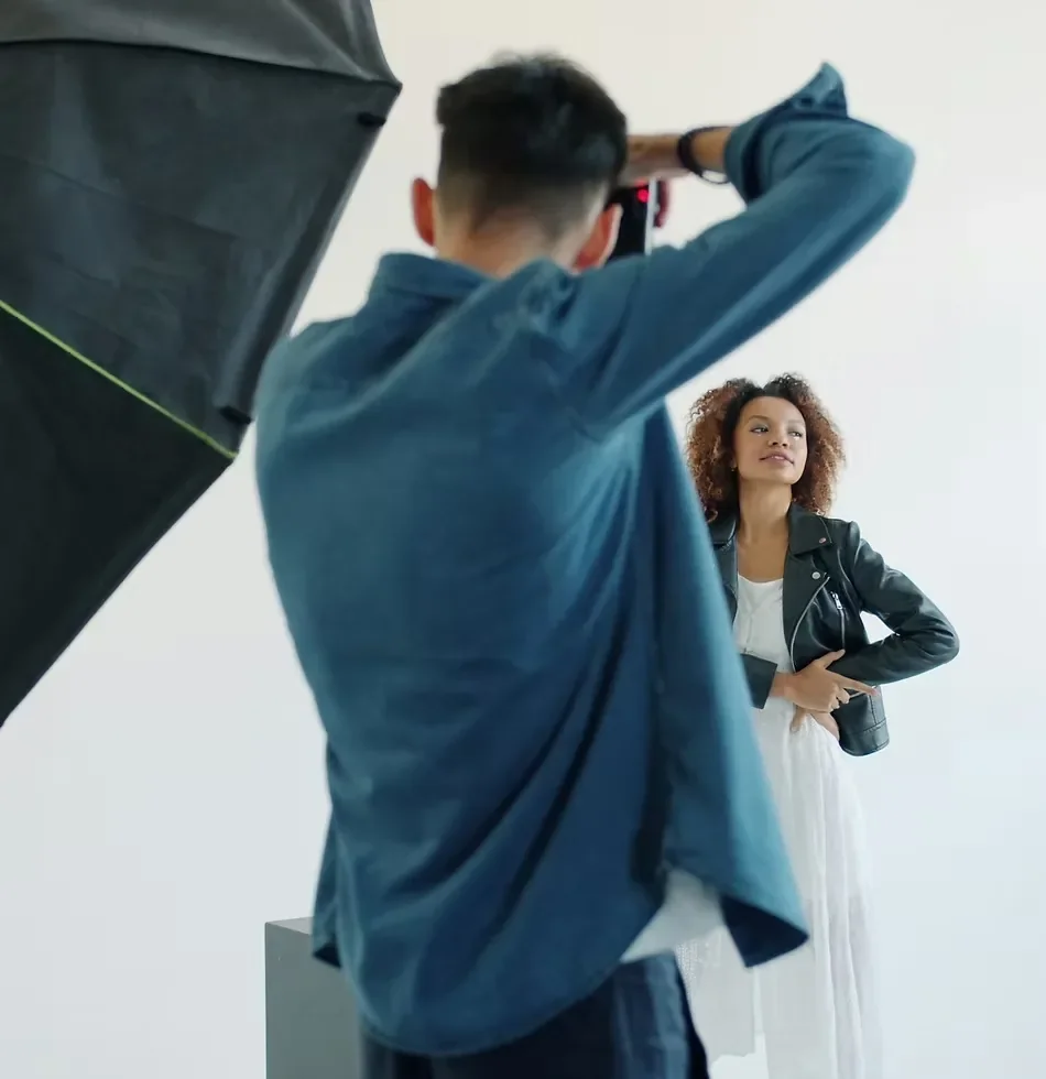 Behind-the-scenes fashion photoshoot featuring a photographer and model against a white cyclorama backdrop in a professional photography studio.