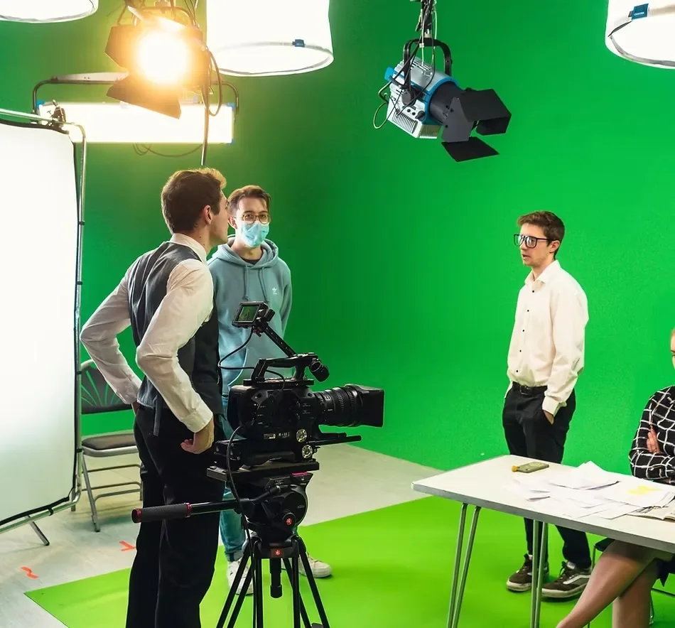 Behind-the-scenes video production featuring a professional cinema camera, studio lighting, and crew working inside a green screen cyclorama studio.