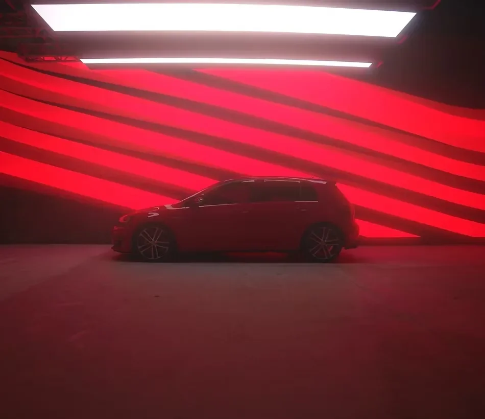 Red Volkswagen car inside an LED volume studio with vibrant red digital backgrounds and overhead lighting panels.