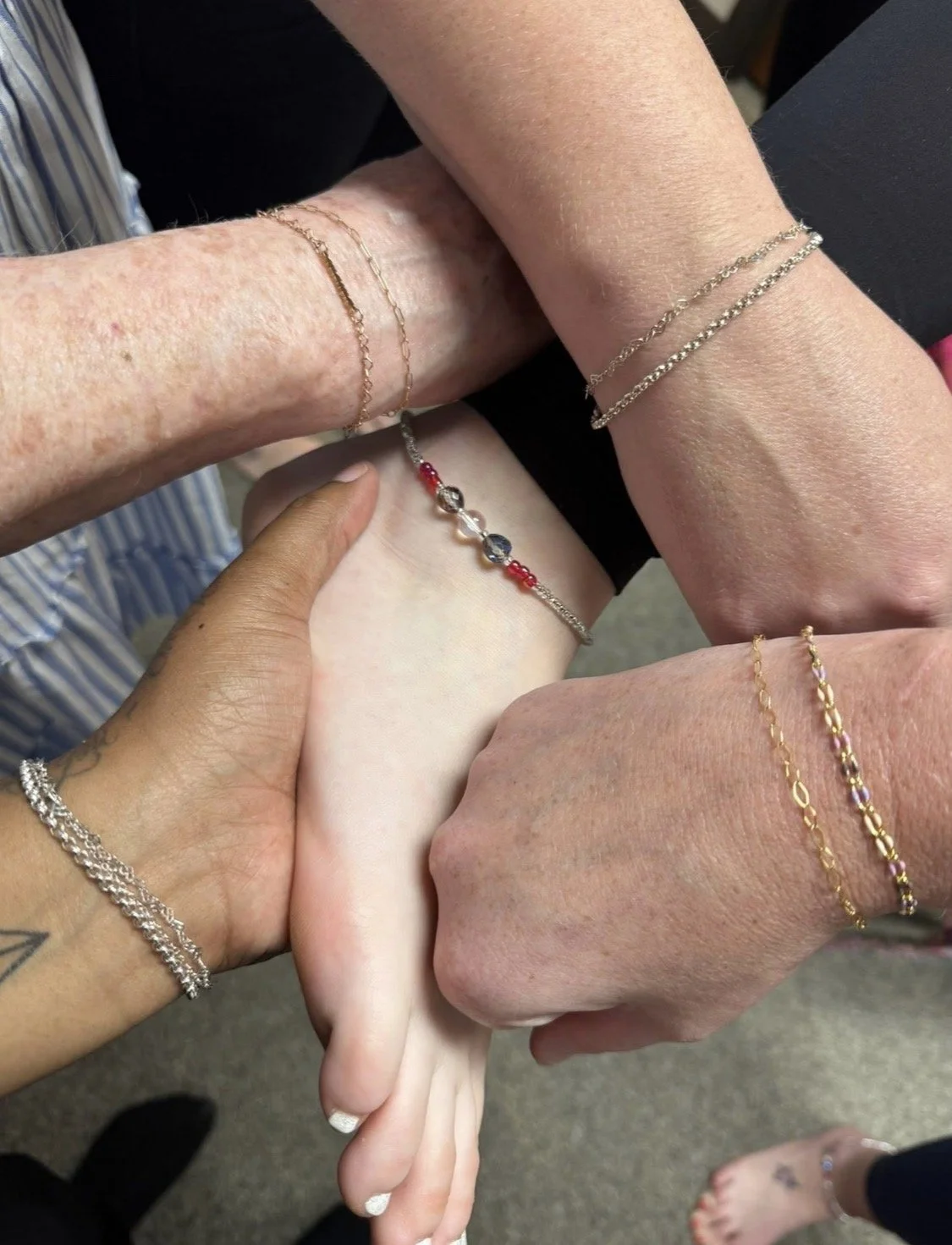 Close-up of two hands holding a small object, against a background of dried flowers. One hand wears a ring and a watch, the other has a tattoo.
