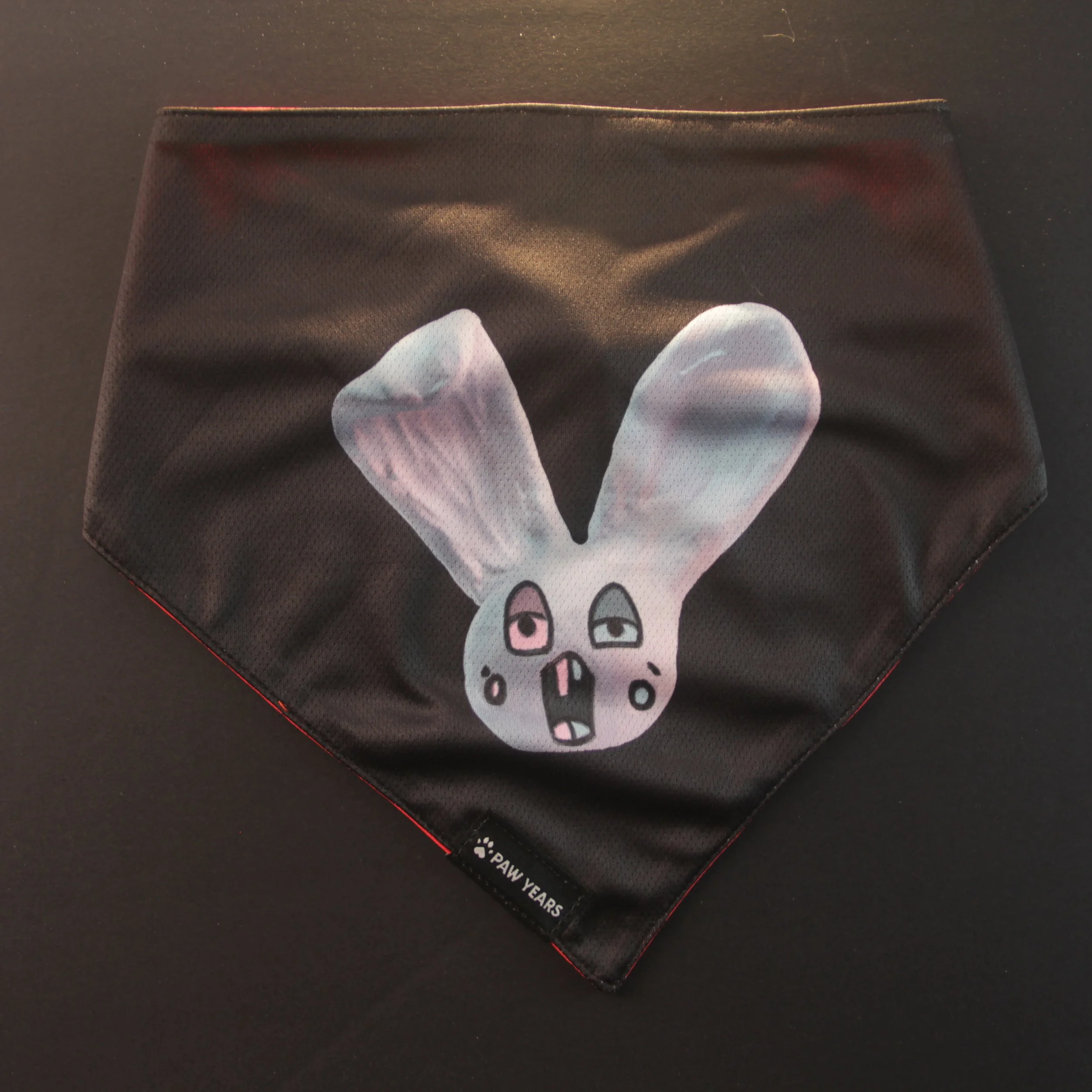 Flat lay of black reversible bandana featuring Loopy blue bunny character with heterochromia eyes.