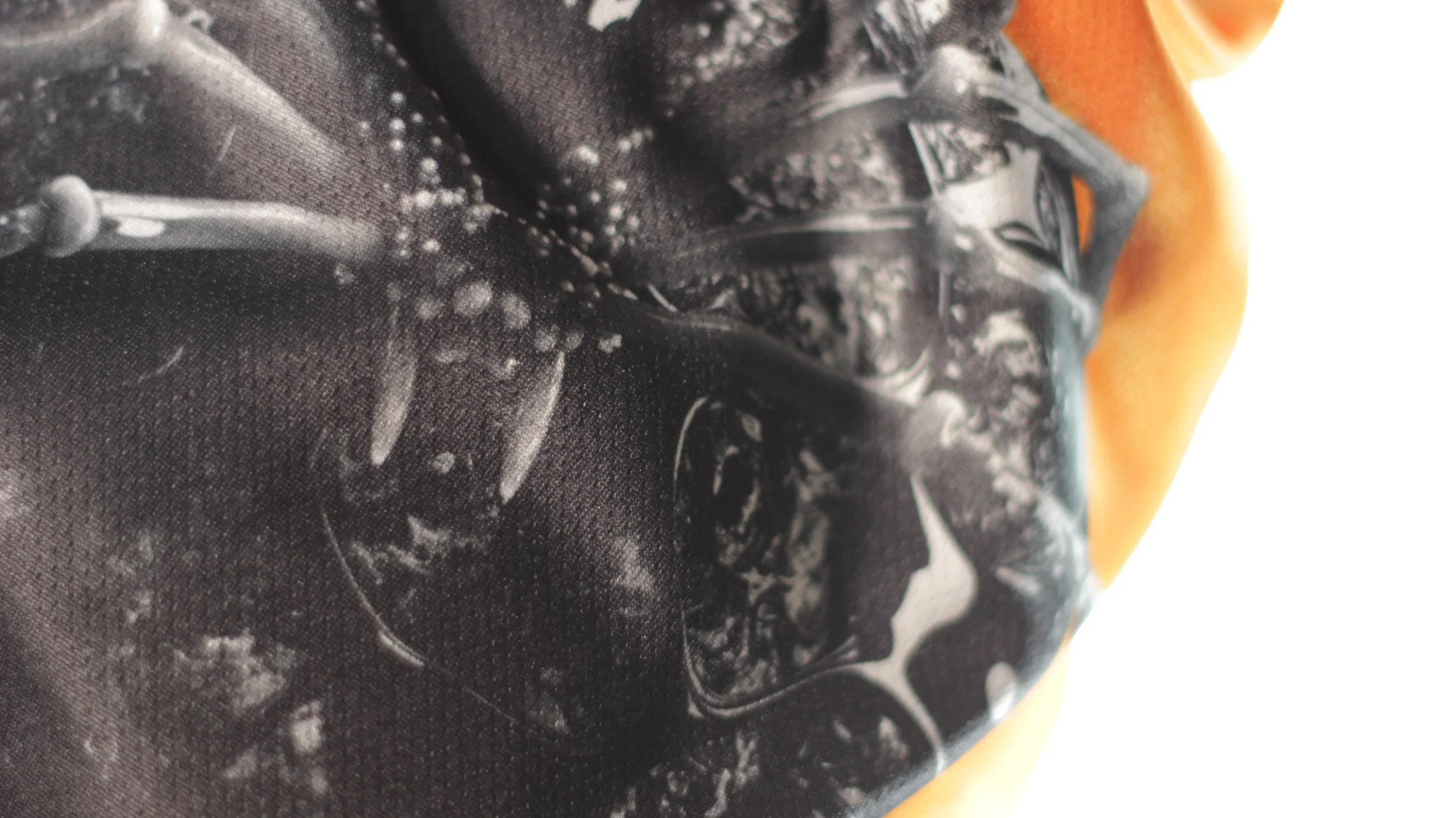 Macro texture detail of black monochrome spider art on orange mesh fabric.