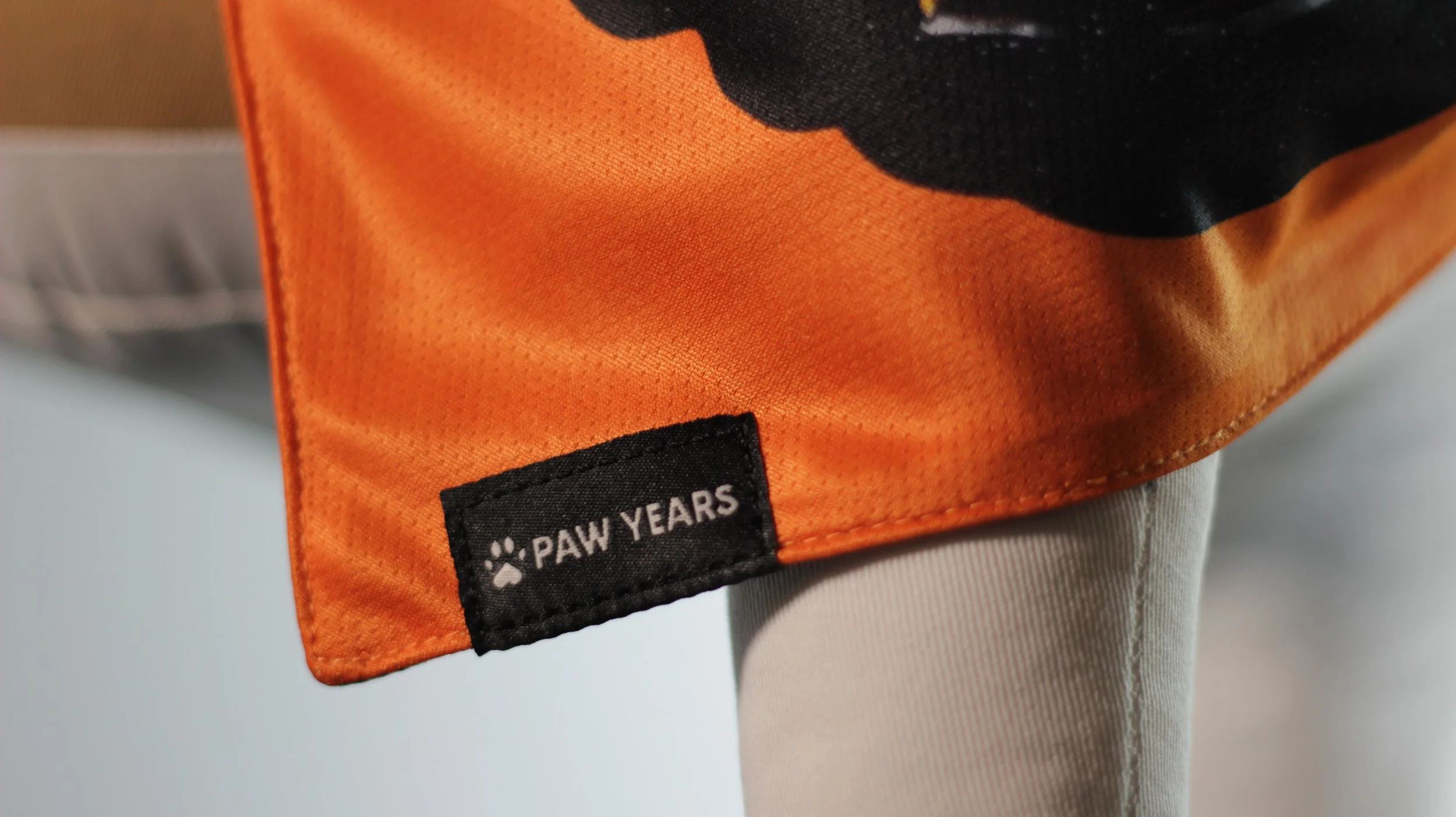Close up detail of Paw Years woven logo tag on the orange side of the limited edition Salem bandana.