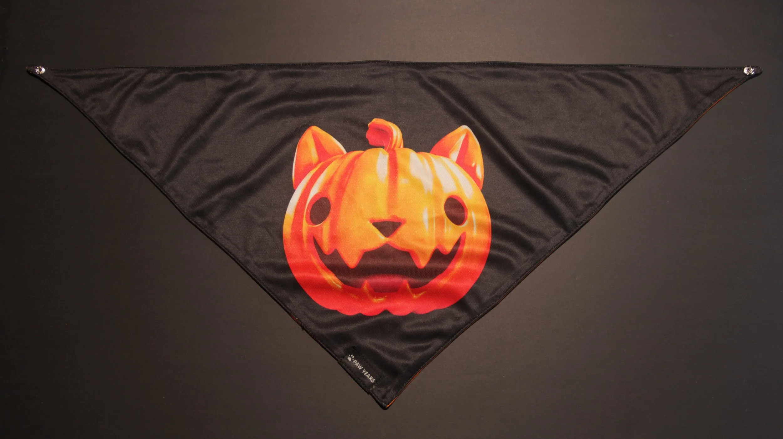 Flat lay of limited edition black Halloween bandana with orange pumpkin face on dark background.