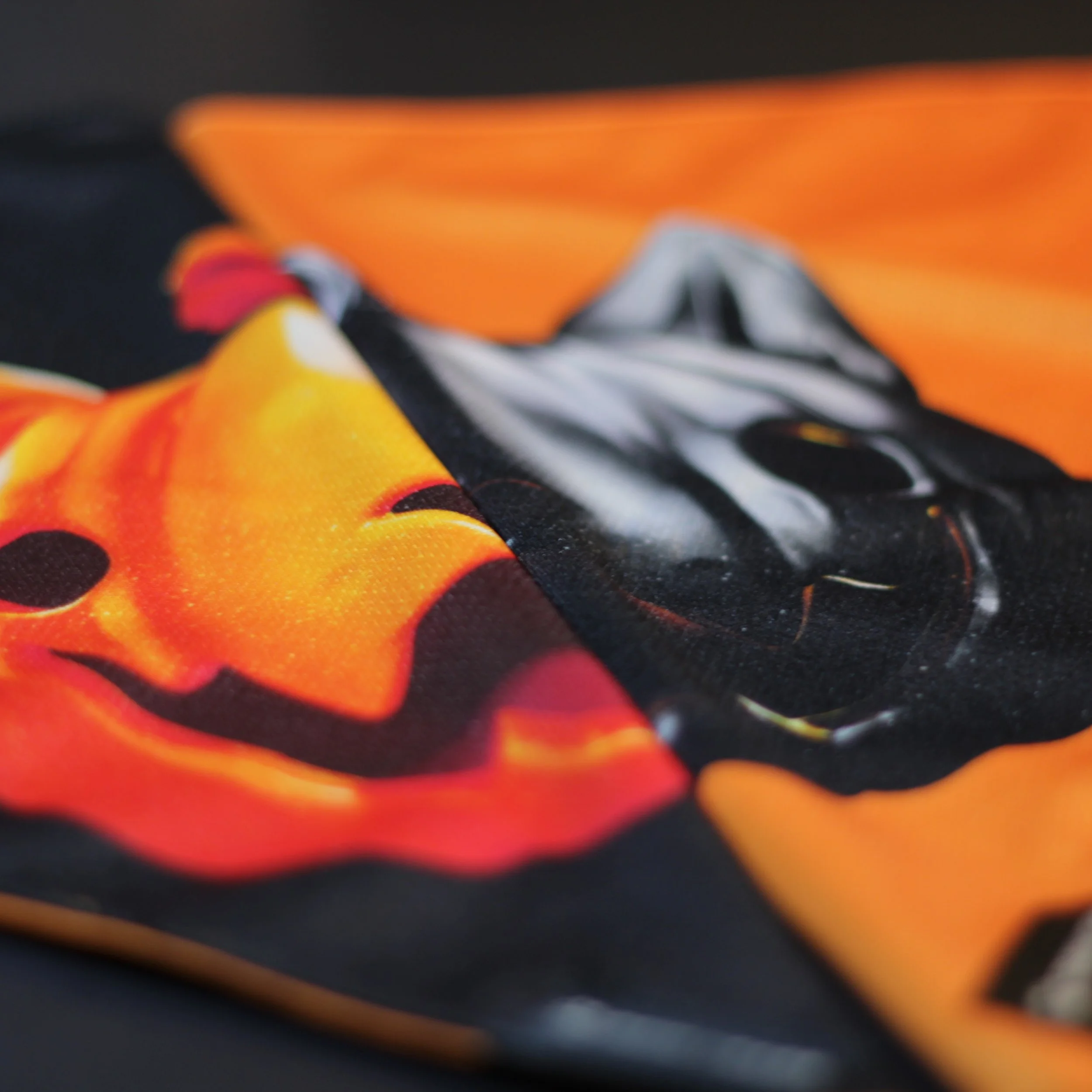Close up detail showing both sides of the Salem reversible bandana with orange and black pumpkin textures.