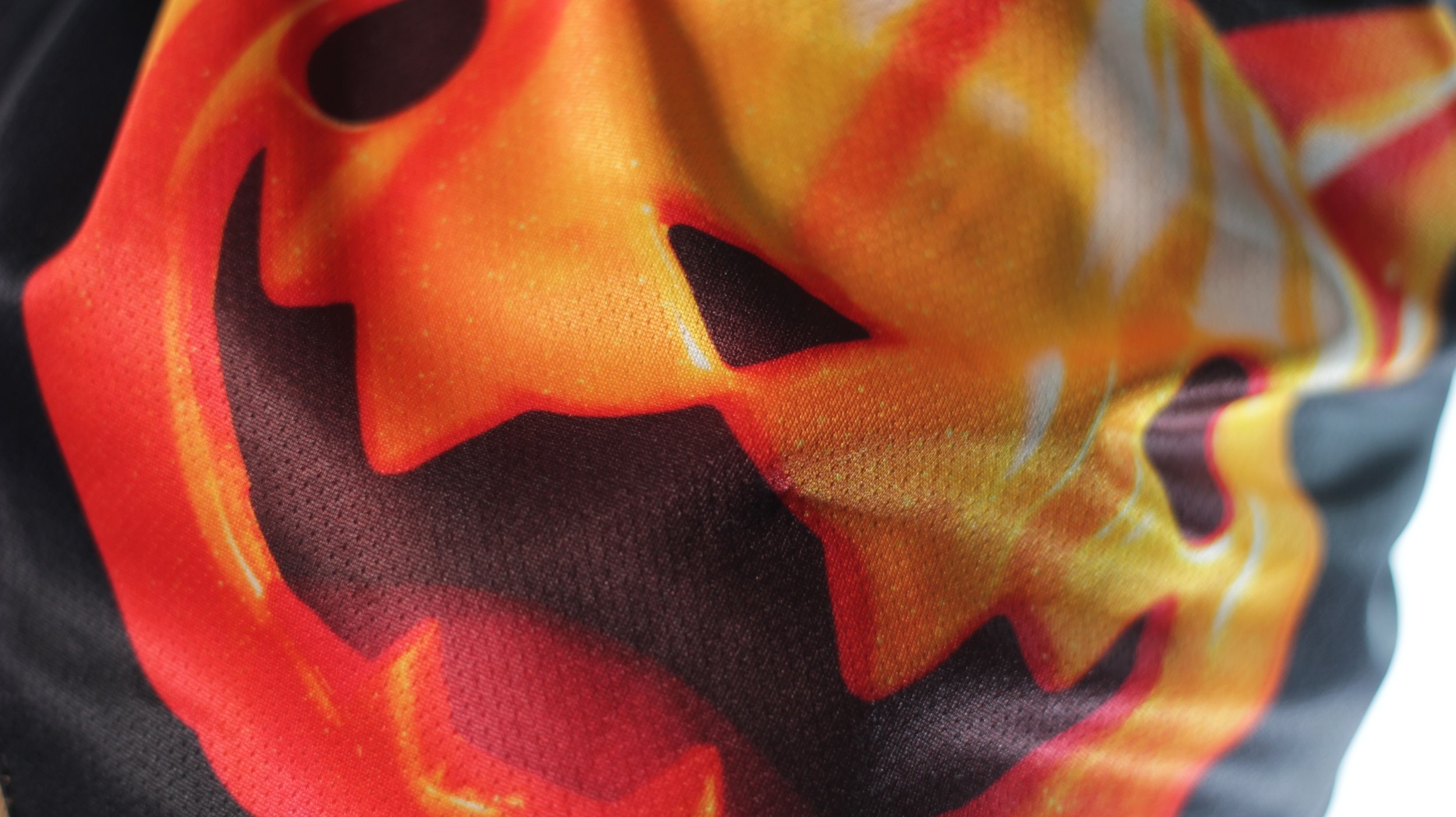 Close up texture shot of glowing orange pumpkin cat art on black mesh fabric.