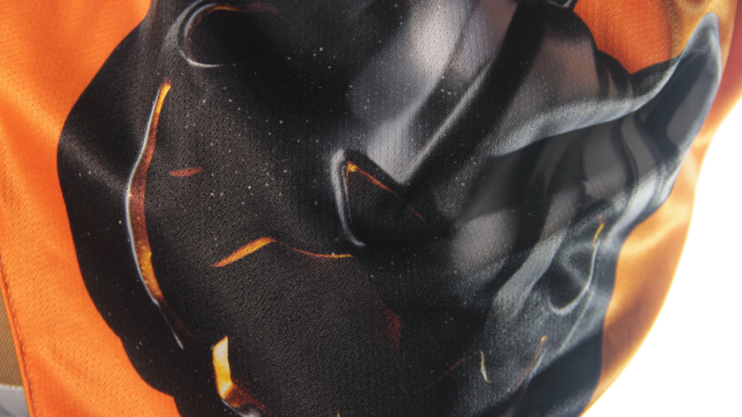 Close up texture shot of obsidian black pumpkin cat art on orange mesh fabric.