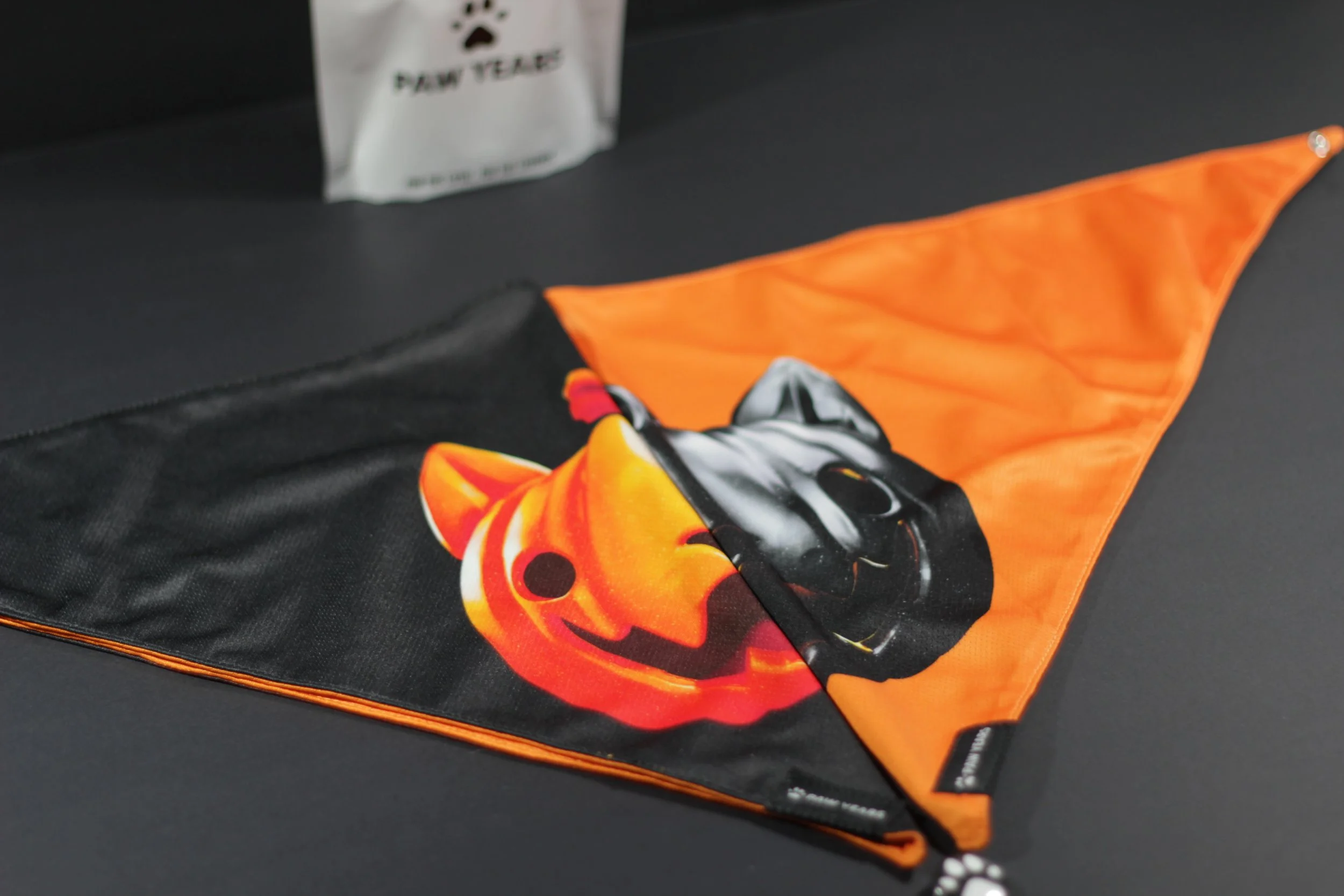 Folded limited edition Salem bandana showing both orange and black sides next to Paw Years packaging.