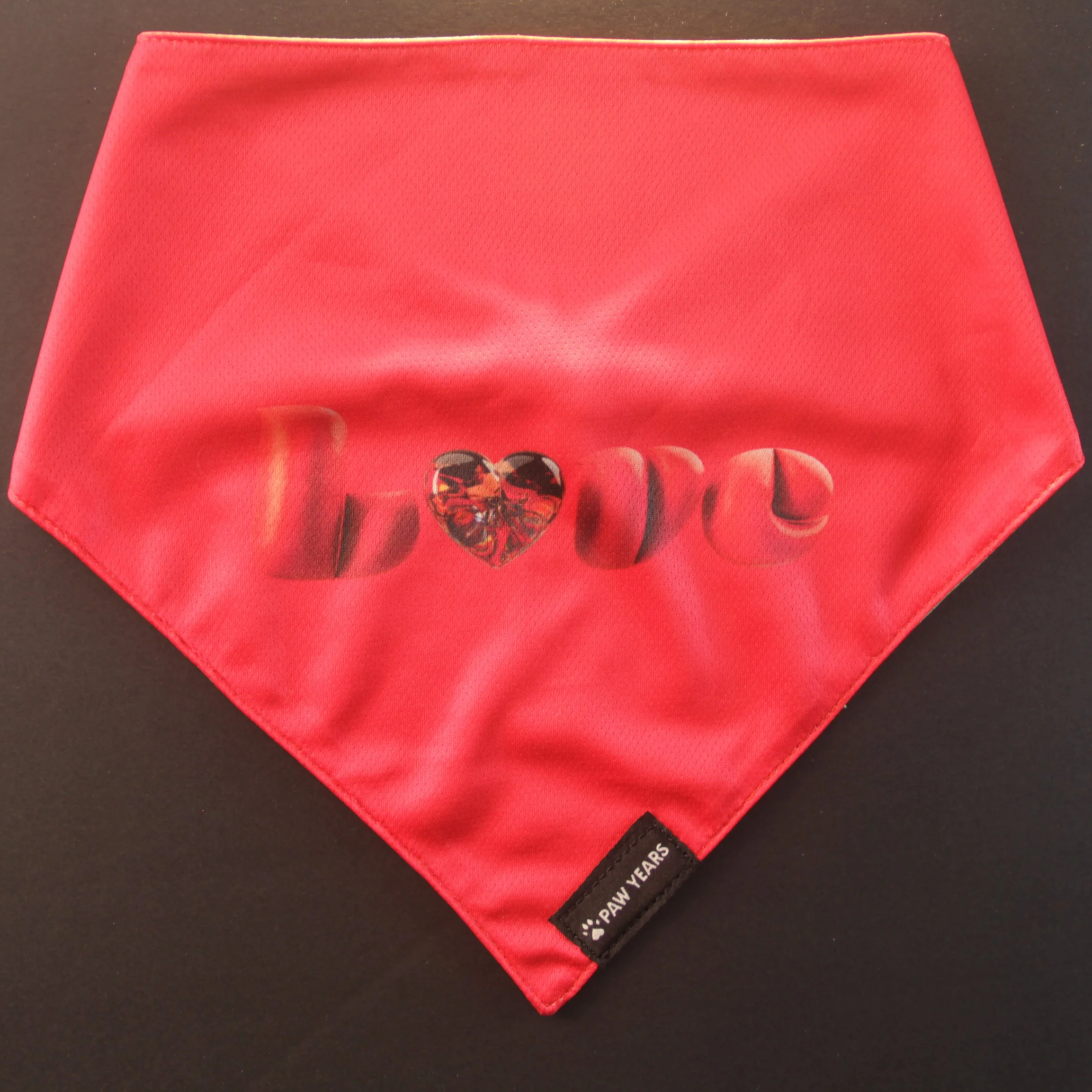 High contrast flat lay of limited edition red Love dog bandana on black background.