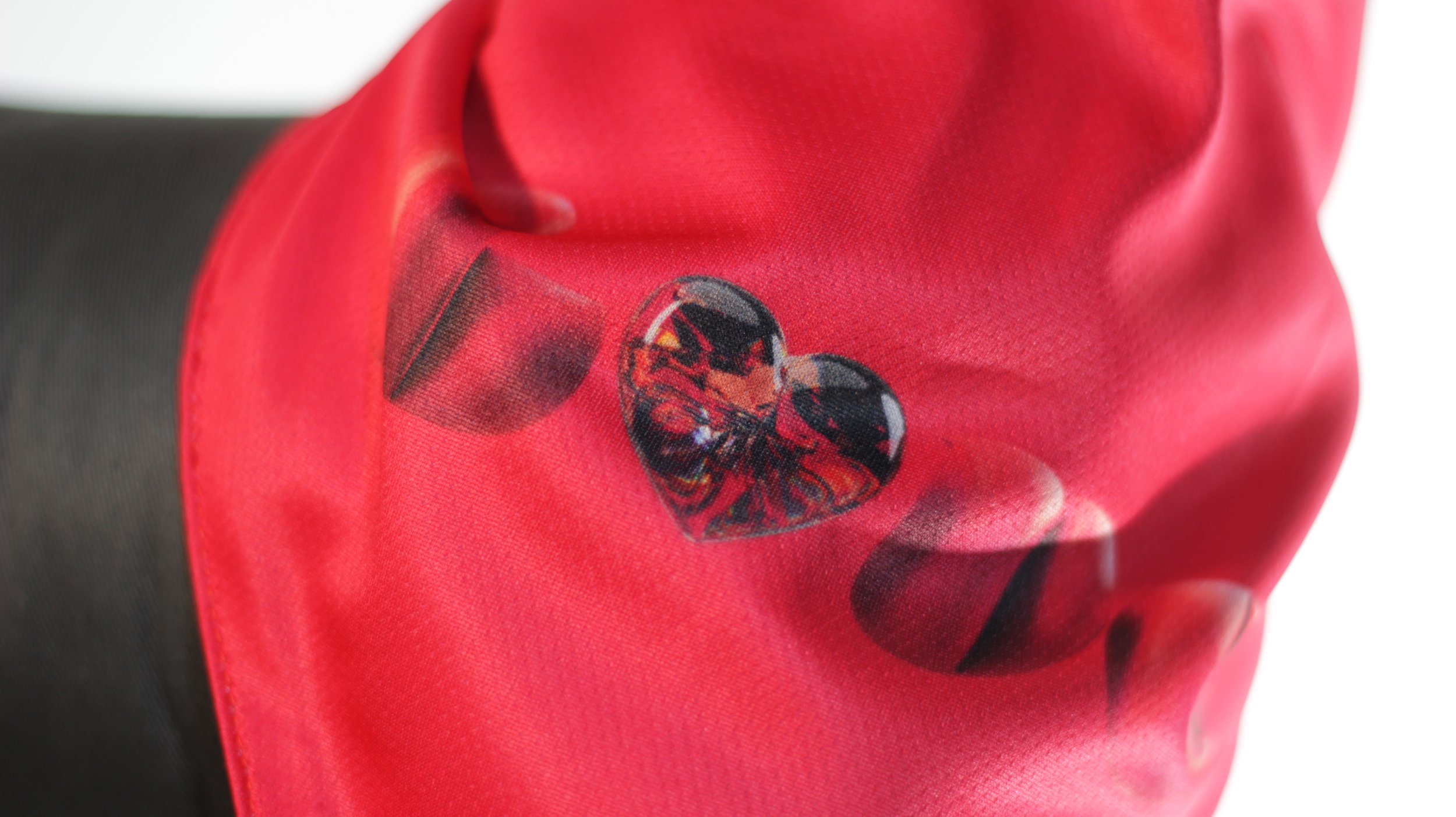 Macro detail shot of faceted ruby heart graphic and red polyester mesh fabric texture on pet bandana.