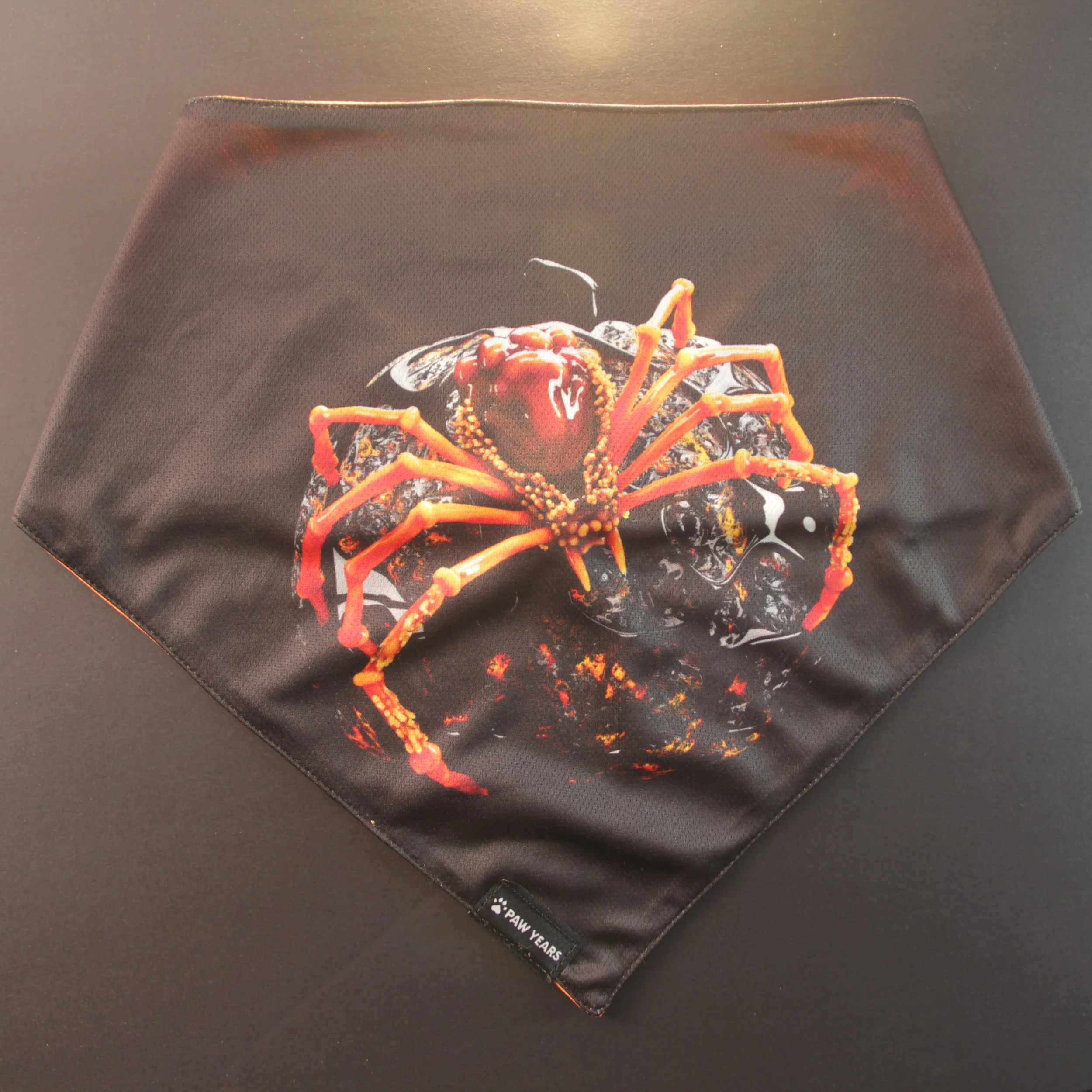 Flat lay of black reversible bandana featuring realistic red and yellow arachnid art.