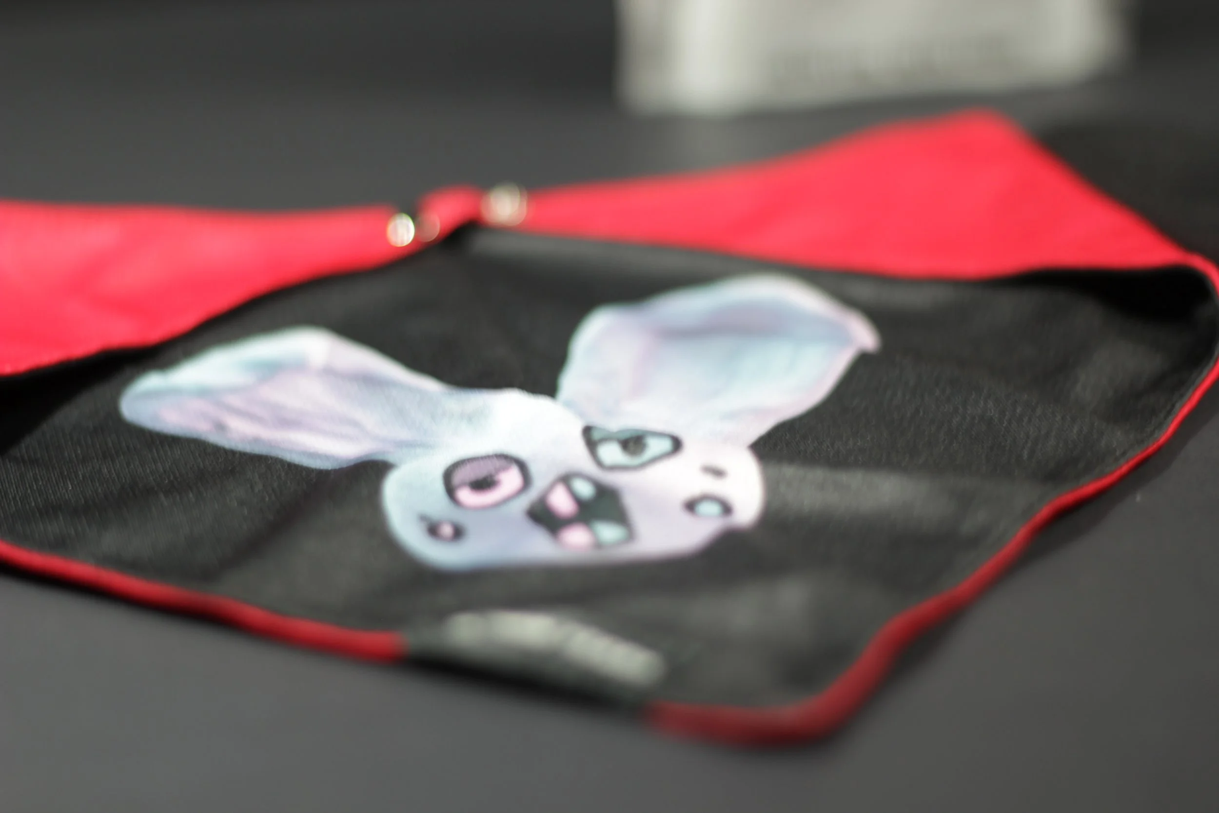 Angled flat lay of the Loopy black bandana showing the blue bunny and reversible red lining.