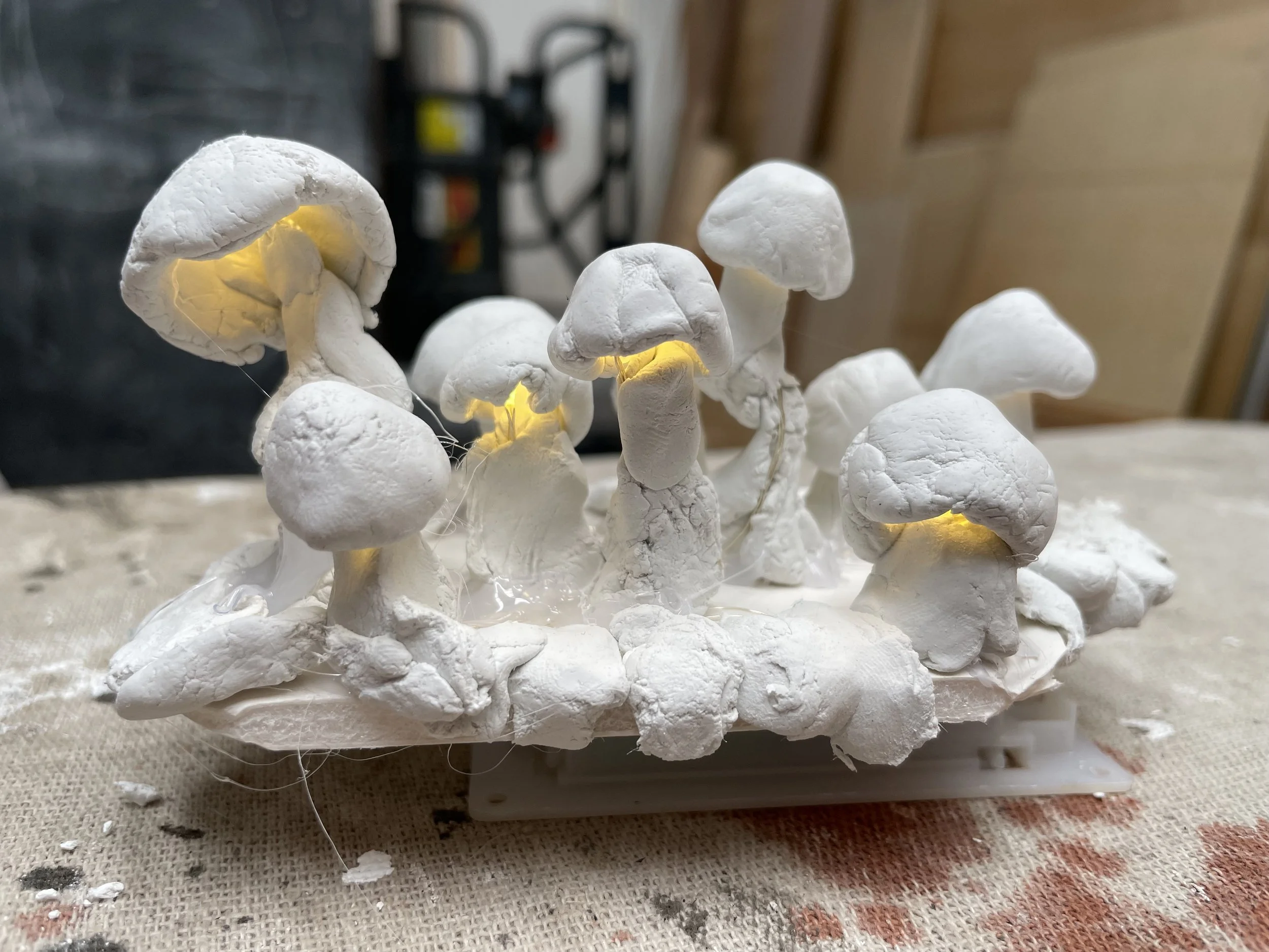 Handmade ceramic mushrooms with illuminated yellow centers arranged on a white base.
