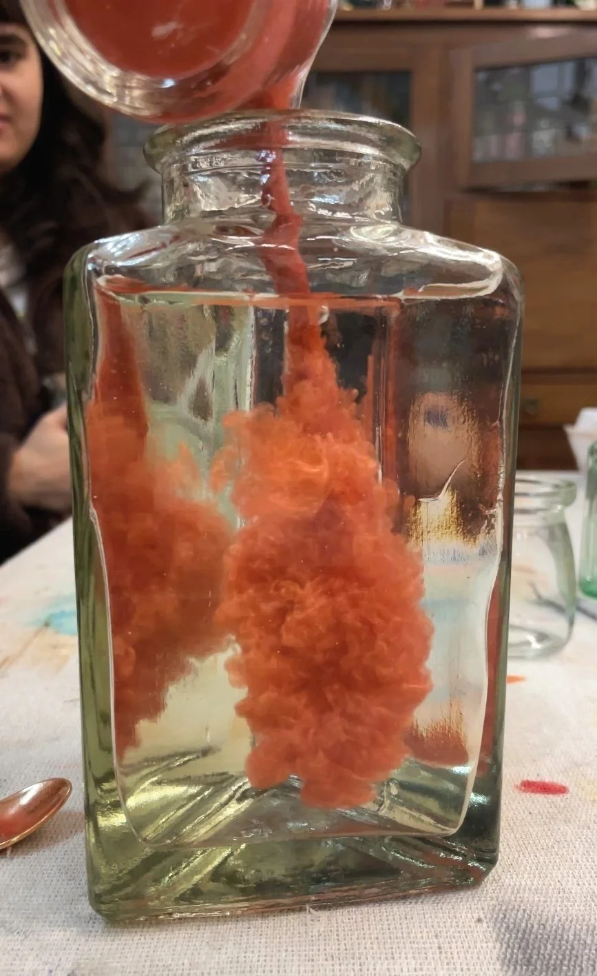A glass jar with water being filled from above, creating orange ink clouds inside the jar.