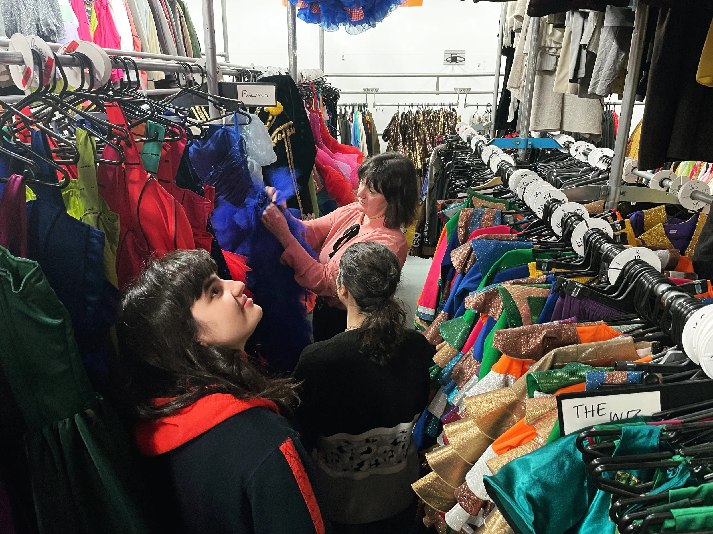 Three women looking through ceiling high racks at a costume warehouse. 