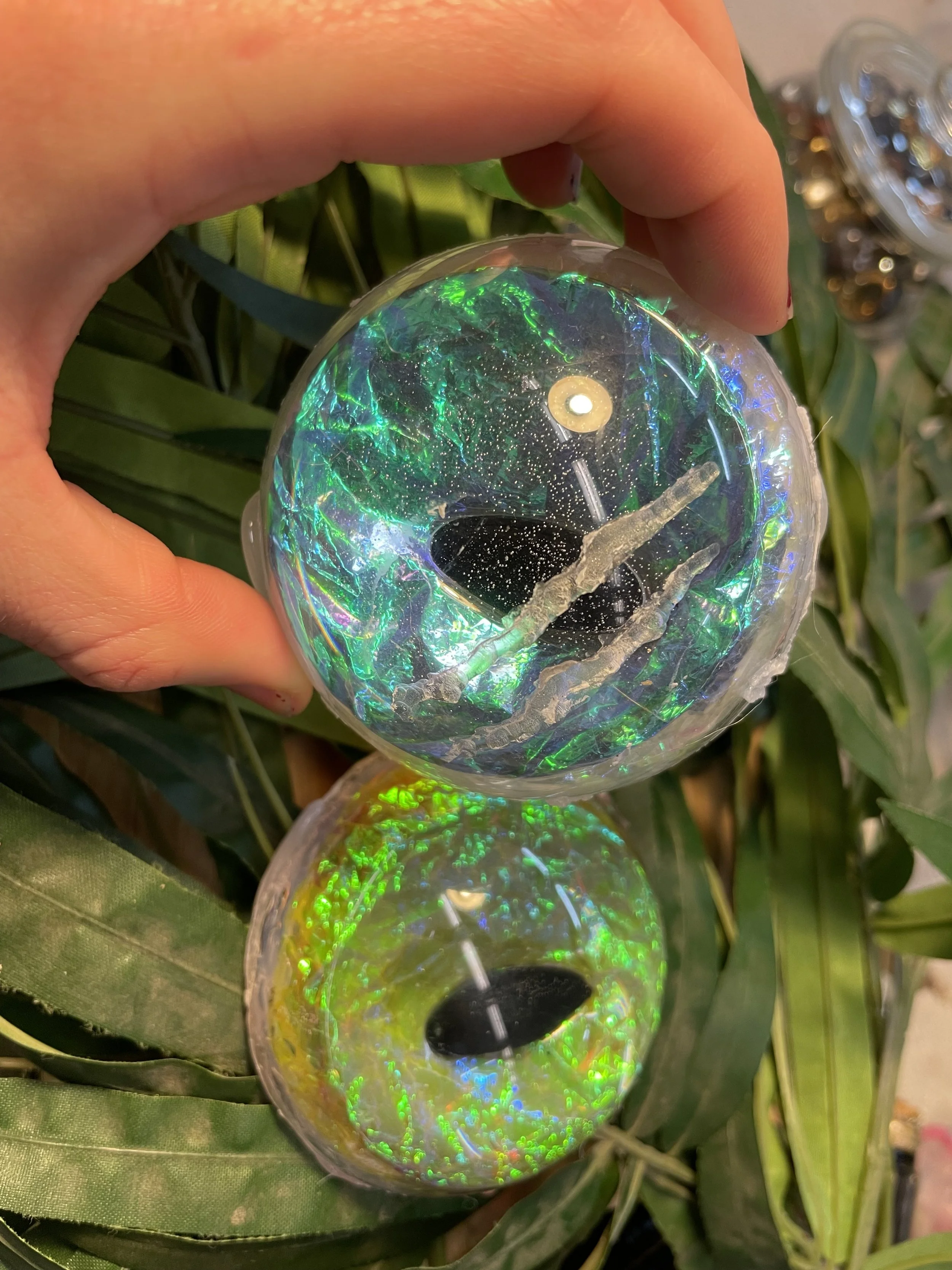 Close-up of a hand holding a dragon eye, with greenery in the background.