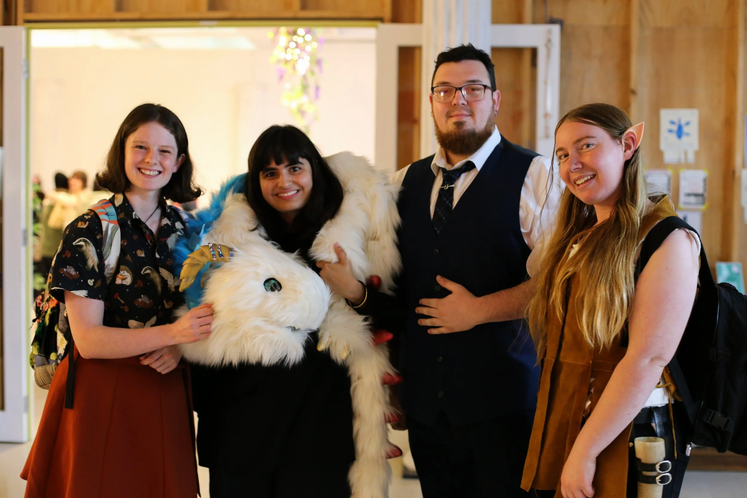 Four people dressed in fantasy costumes, standing with a person in a unicorn costume at an indoor event or convention.