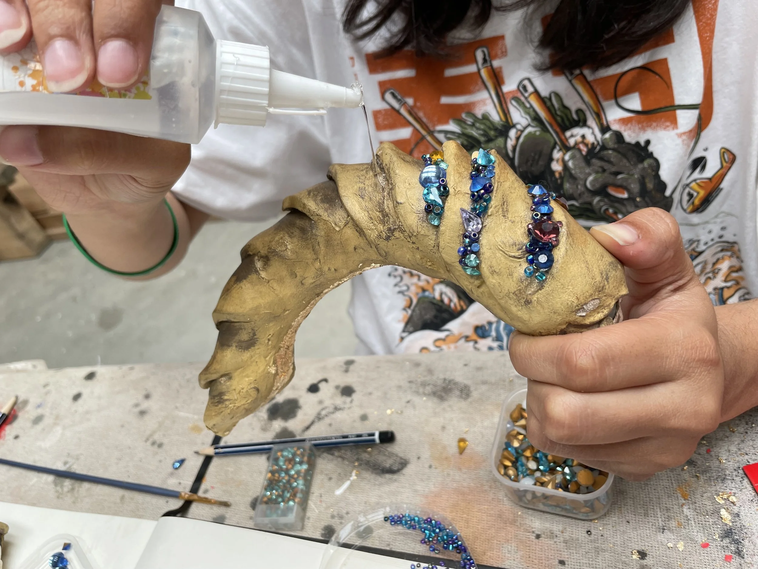 Person working on jewelry making, attaching blue and purple gemstones to a bracelet or ring on a decorative piece that resembles a buffalo skull.