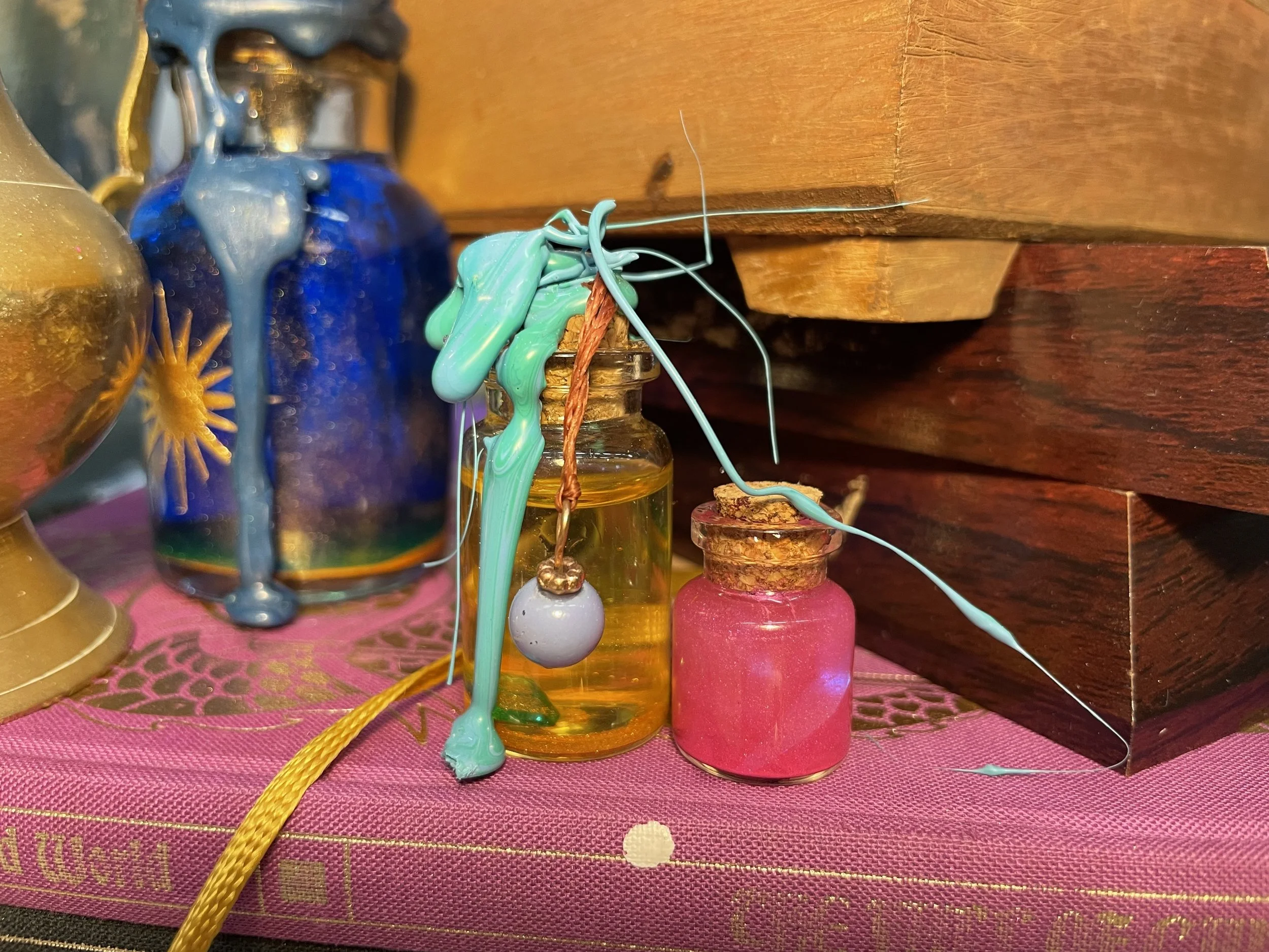 Small glass bottles with colorful liquids and wax drippings, placed on a pink cloth with a wooden background.