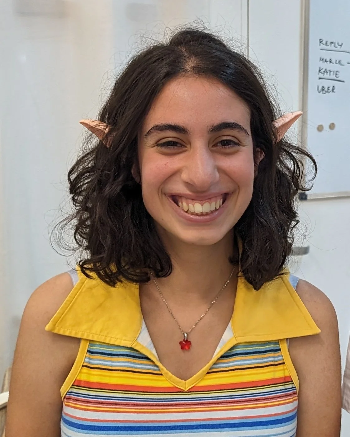 A woman smiling with elf ears and a rainbow striped top.