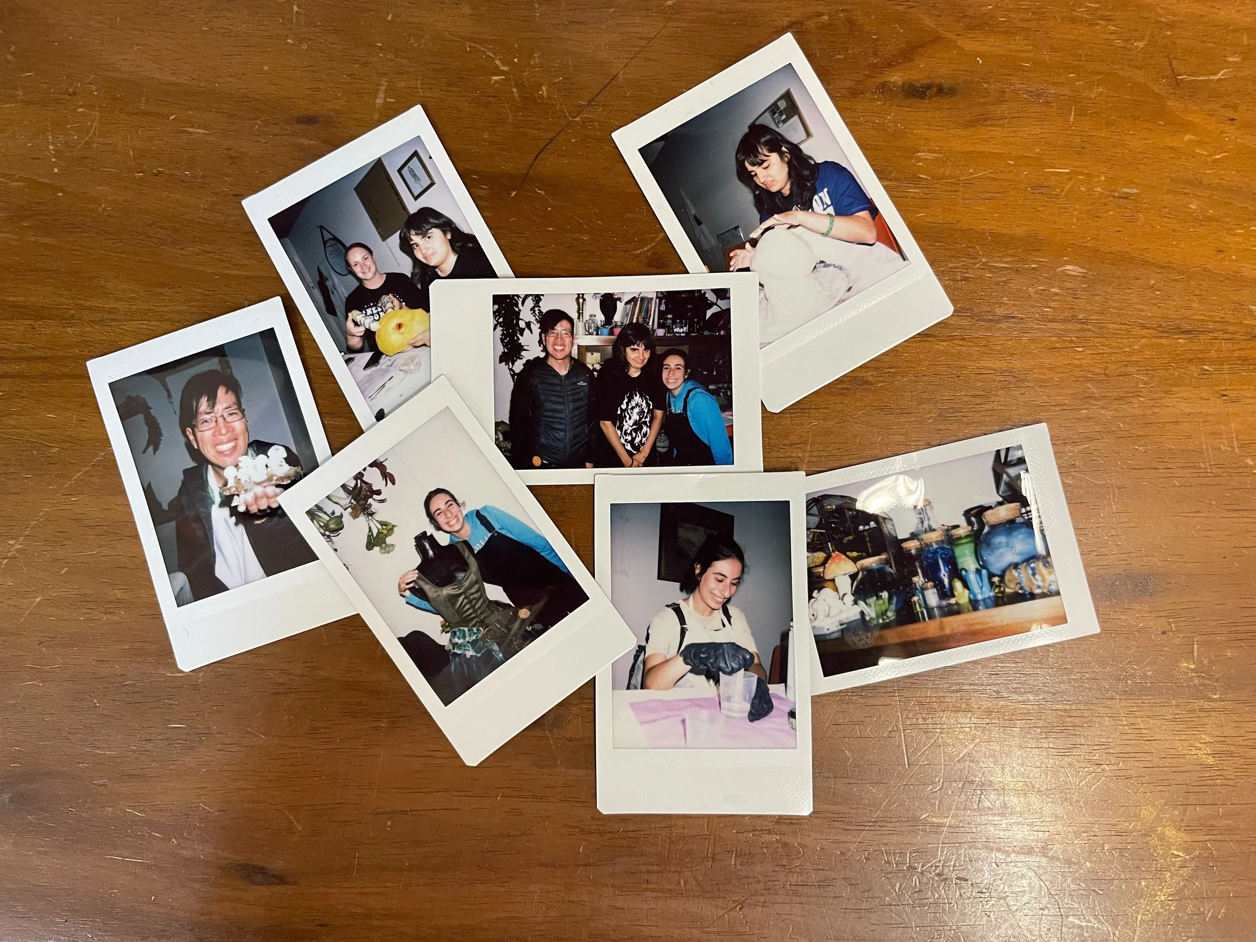 Multiple fluorescent photo prints of various people, including a woman holding a head of lettuce and three women smiling together, scattered on a wooden surface.