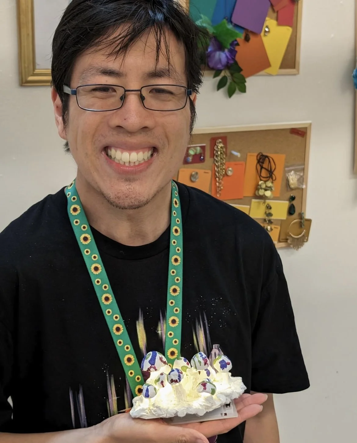 Man smiling and holding a light up mushroom sculpture, wearing glasses and a sunflower patterned lanyard.