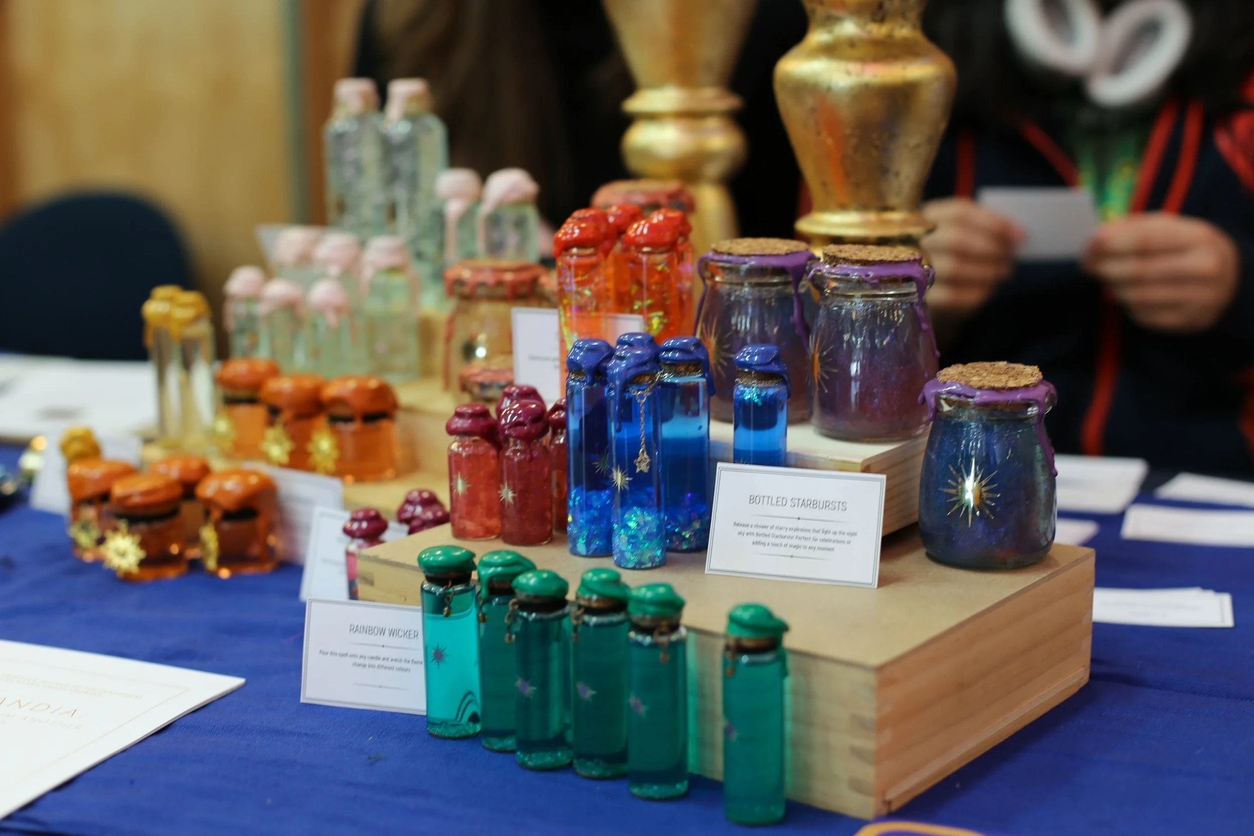 Colorful glass bottles displayed on a wooden stand at a craft fair.
