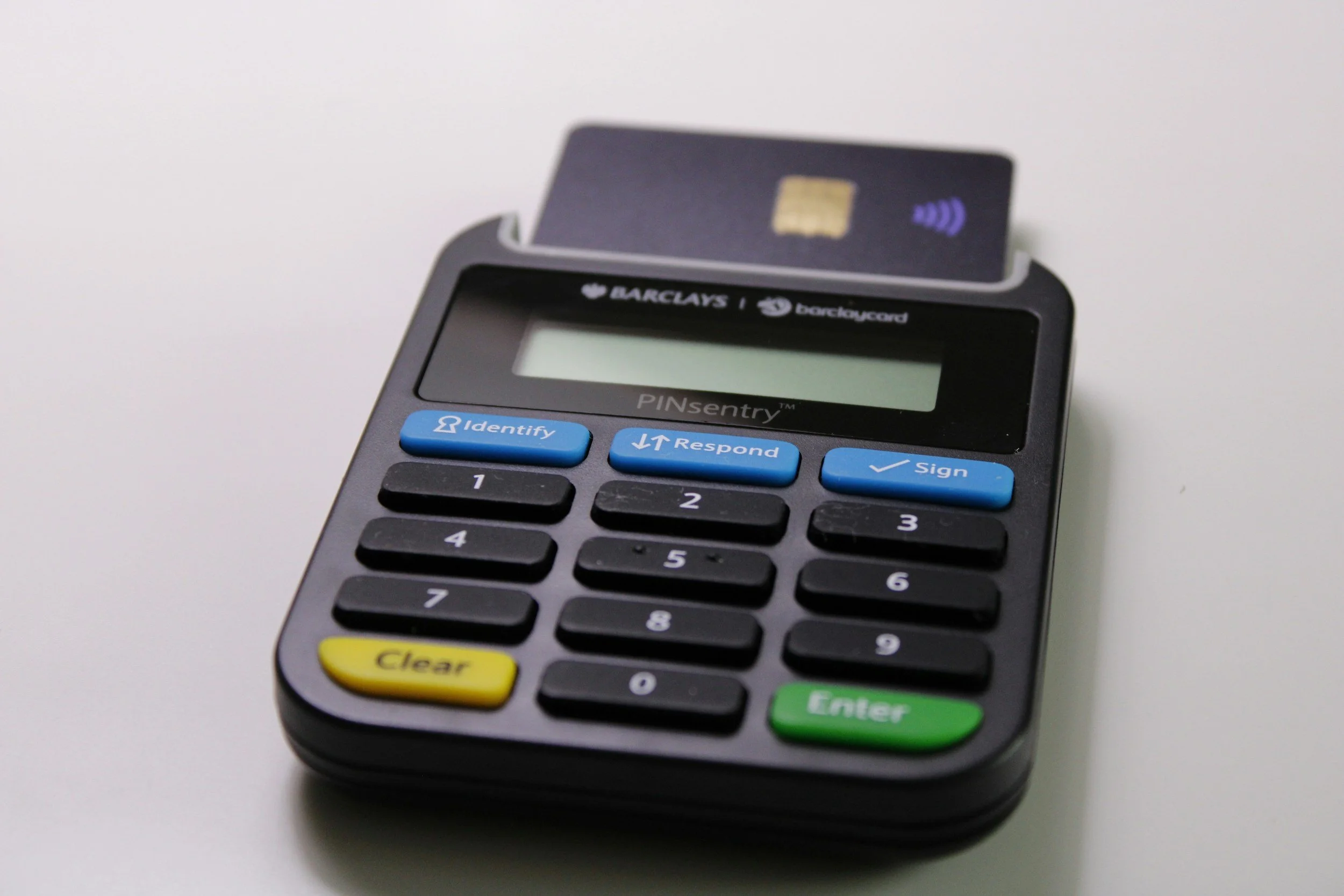 A portable card reader with a credit card inserted. The device has labeled buttons including 'Identify,' 'Respond,' and 'Sign,' and colored keys such as yellow 'Clear' and green 'Enter.'