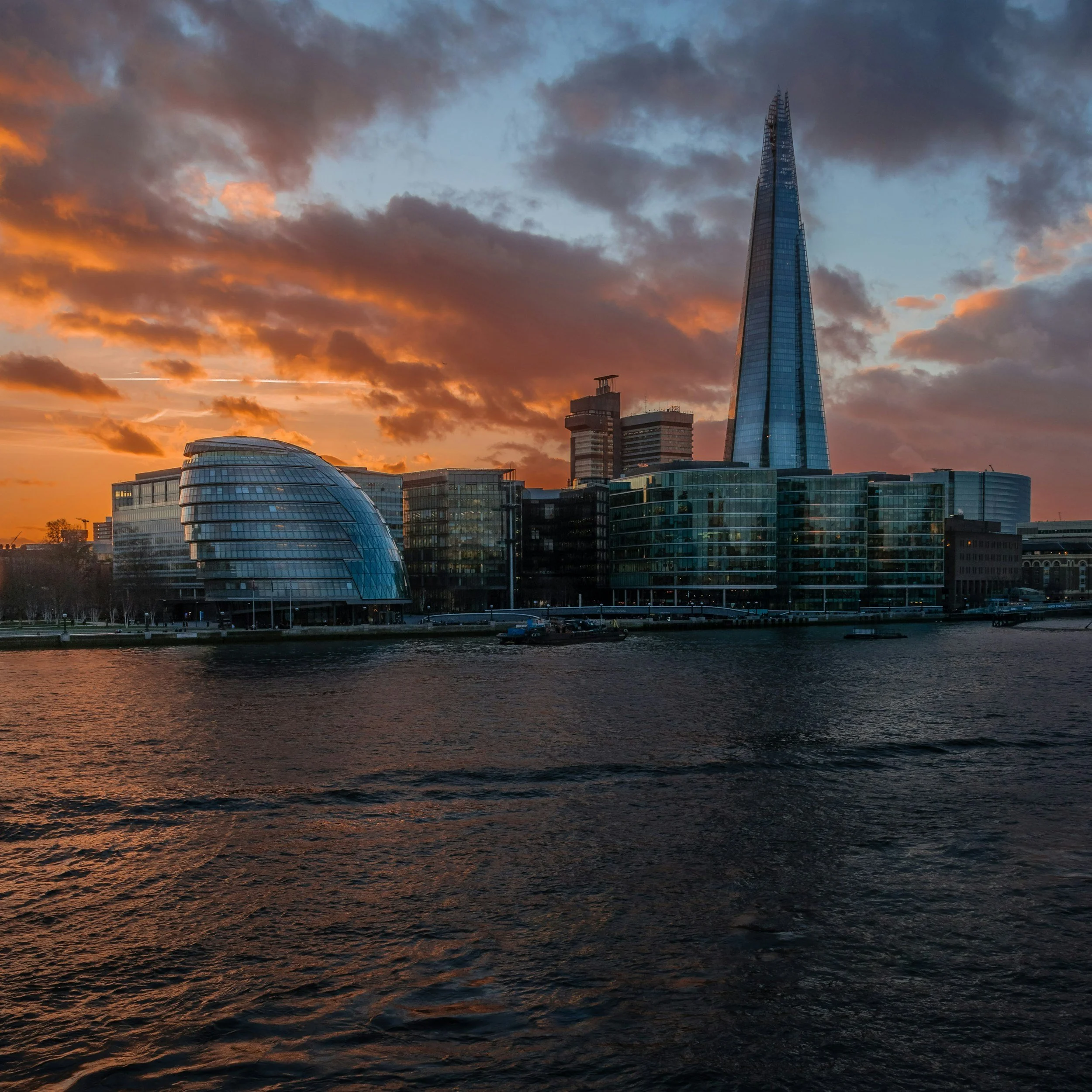 A city skyline at sunset with modern glass skyscrapers and clouds in the sky.