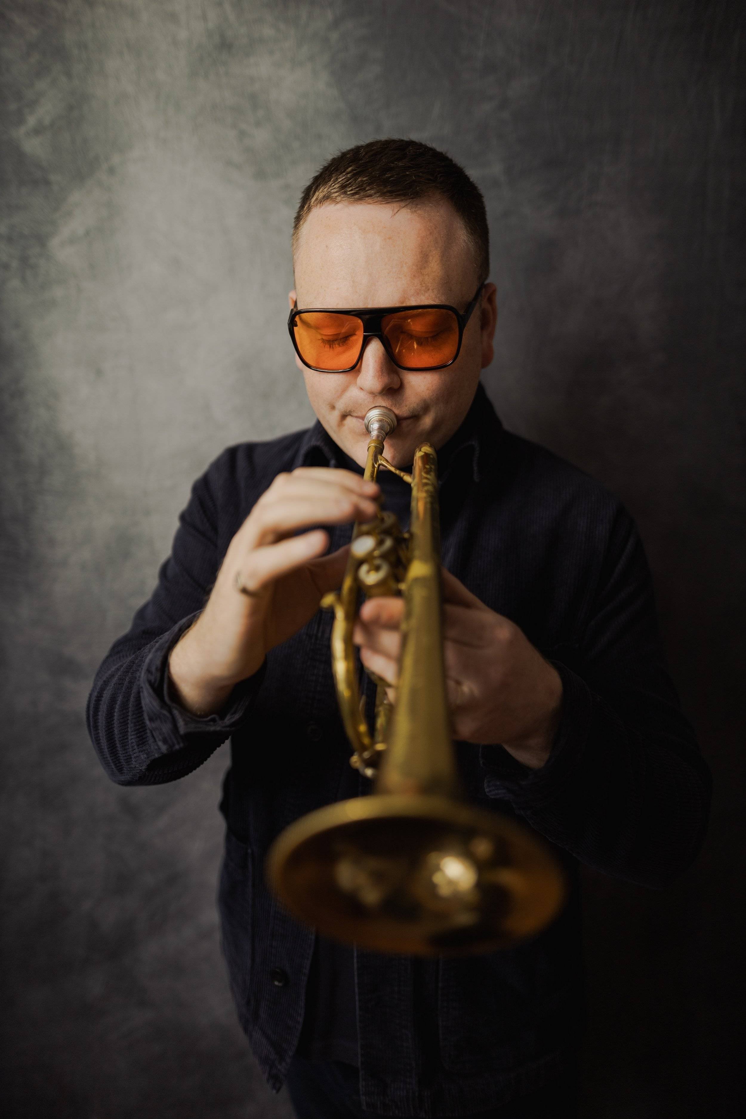 A man wearing red sunglasses plays a jazz trumpet