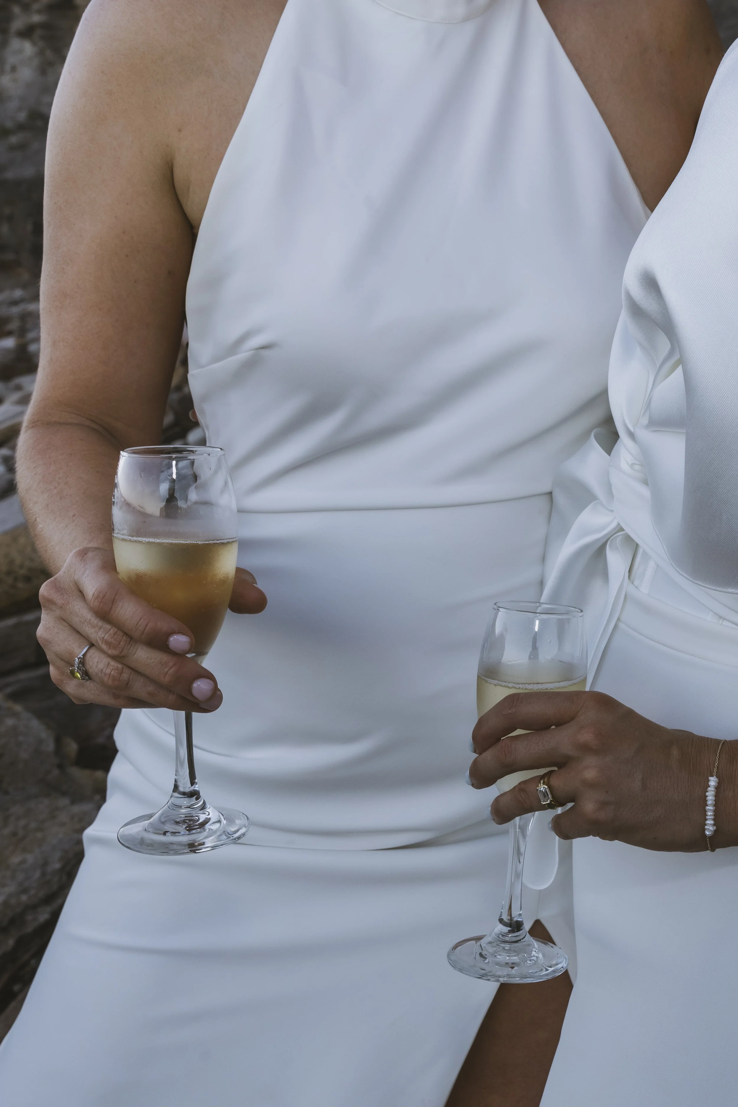Two women in white dresses holding glasses of champagne, possibly celebrating.