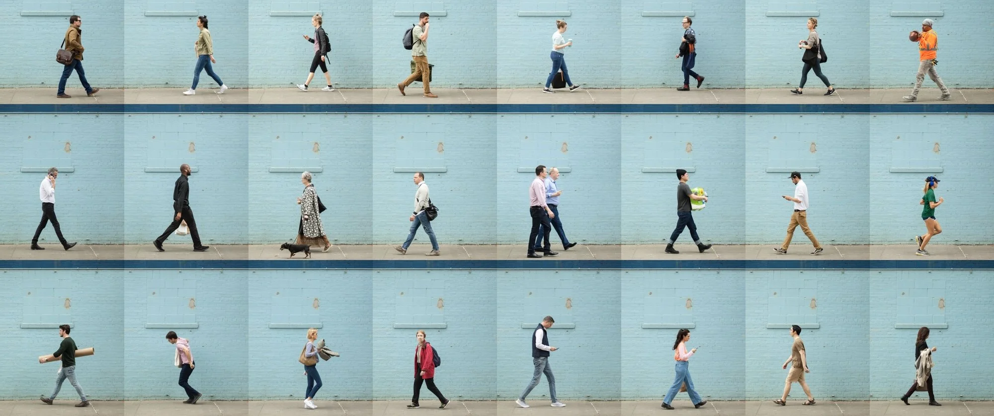 Multiple people walking along a sidewalk in front of a light blue wall, each engaged in different activities such as talking on the phone, listening to music, or looking at their phones, some with bags or backpacks.