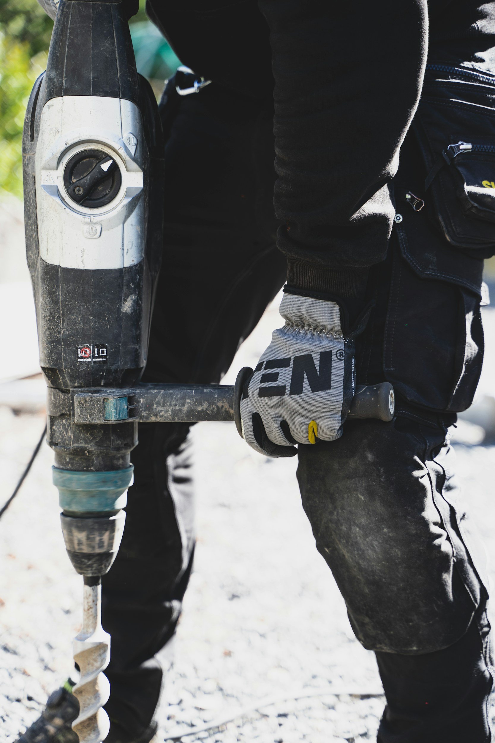 Close-up of a person operating a cordless power drill outdoors with snow on the ground, wearing a black jacket and gloves