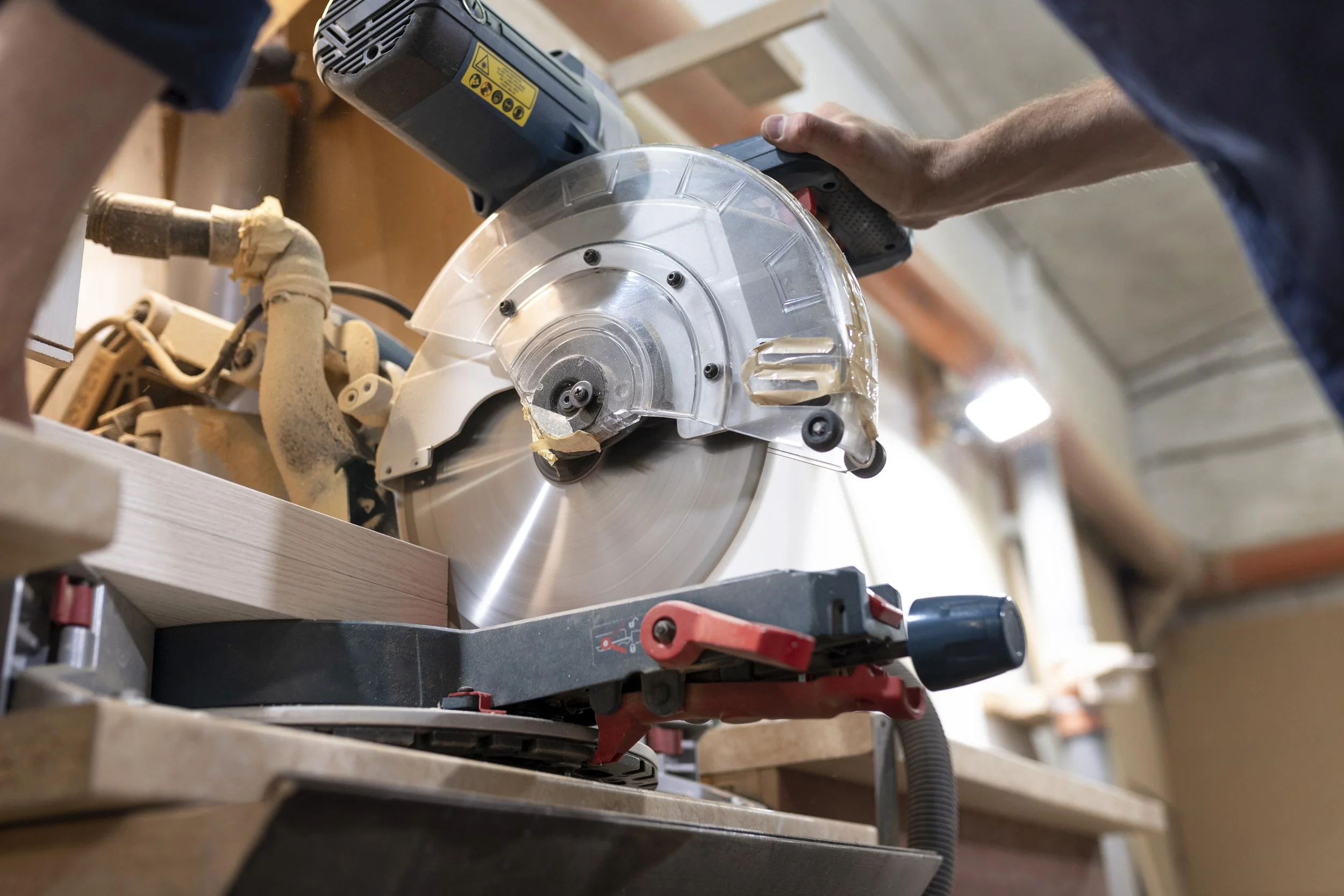 A person using a power miter saw to cut a piece of wood in a woodworking workshop.