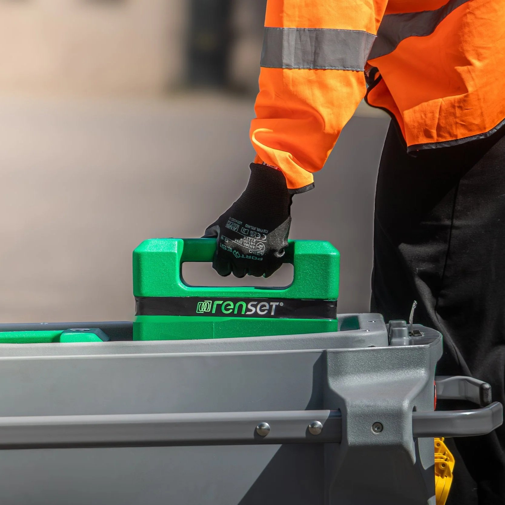 A person holding a large green battery pack next to a smaller green battery pack, both placed on a black Renset battery management system device.