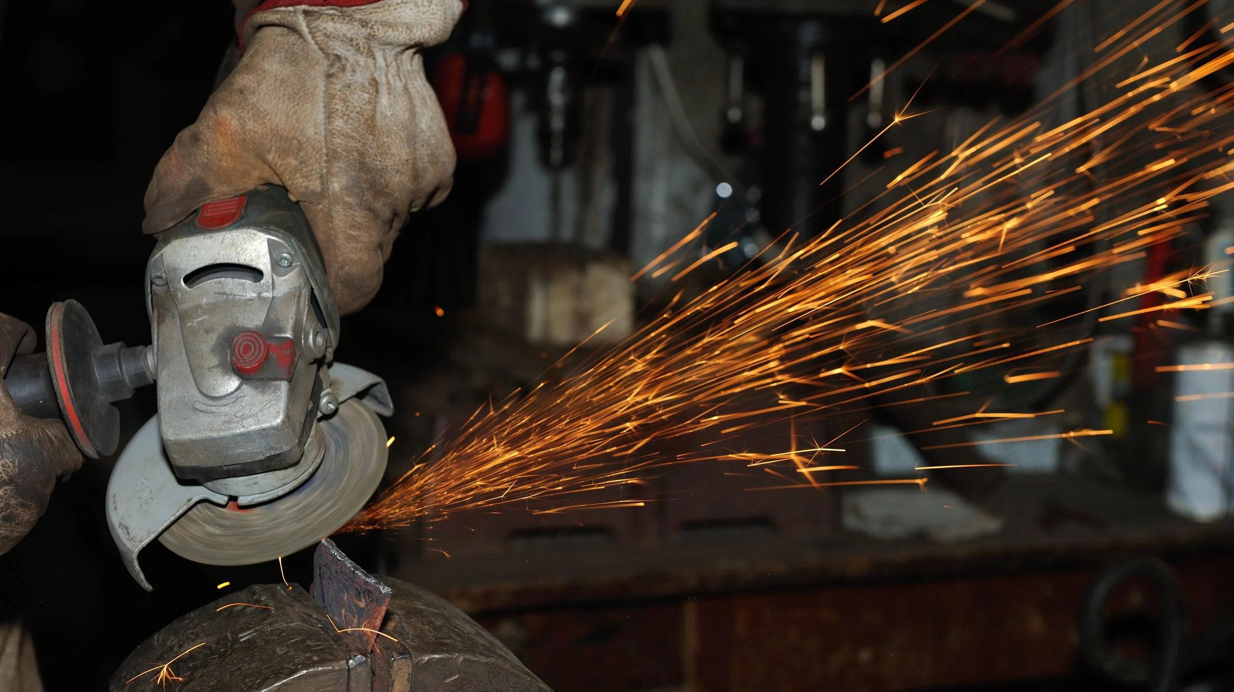 A person wearing protective gloves using an angle grinder on a metal pipe, producing sparks.