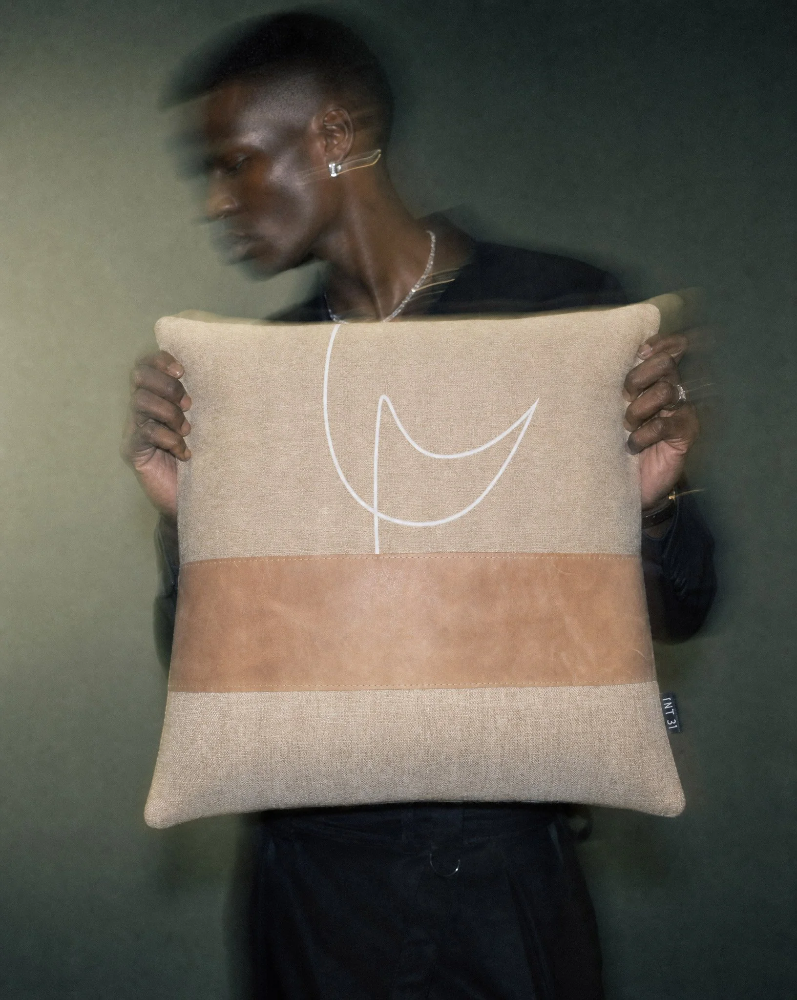 Generated-with-Kive.ai---male-model-hands-with-dark-skin-lightly-holding-the-edges-of-a-20-x-20-inch-cushion-spanning-the-full-width-of-the-torso_-from-shoulder-to-shoulder.-Model-is-wearing-dark-monochrome-menswear-with-architectural-silho.jpg