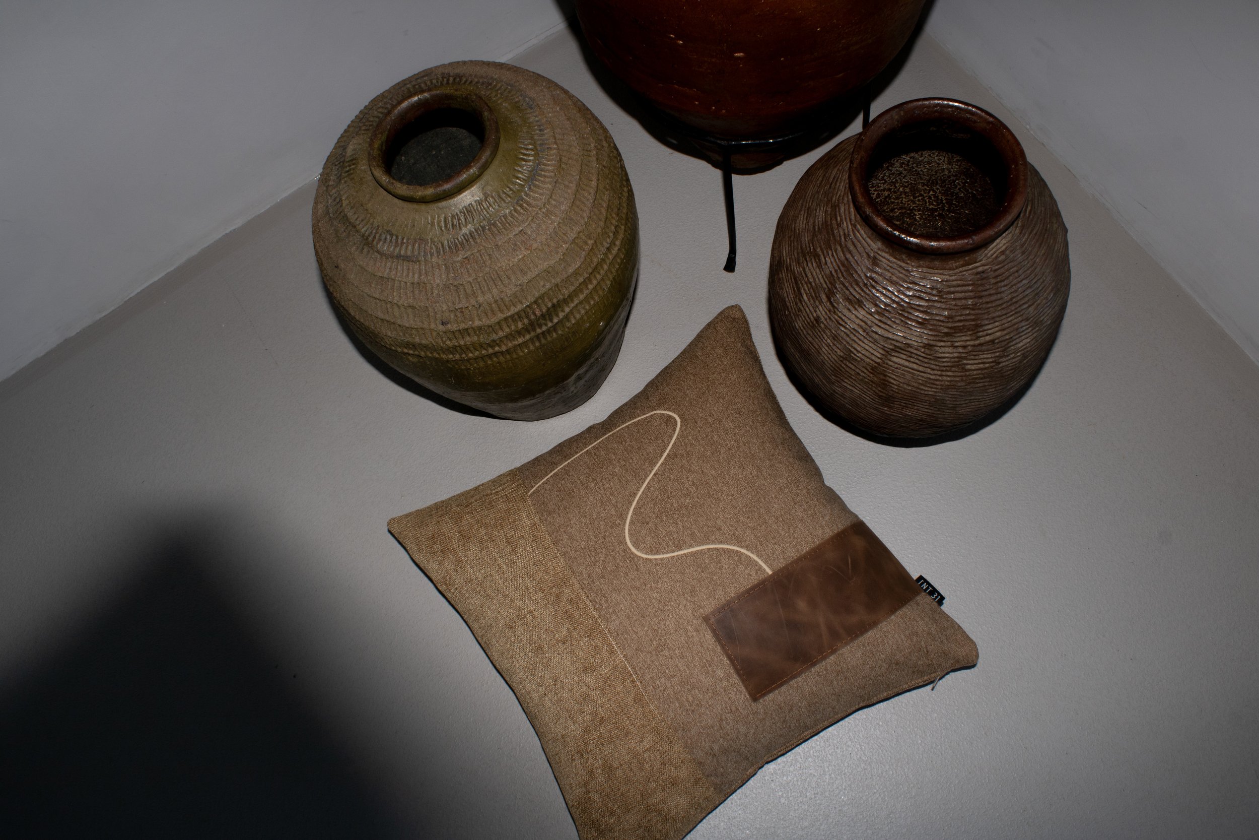 Three clay pots of varying sizes and colors arranged on a beige surface with a brown pillow, some with visible textures.
