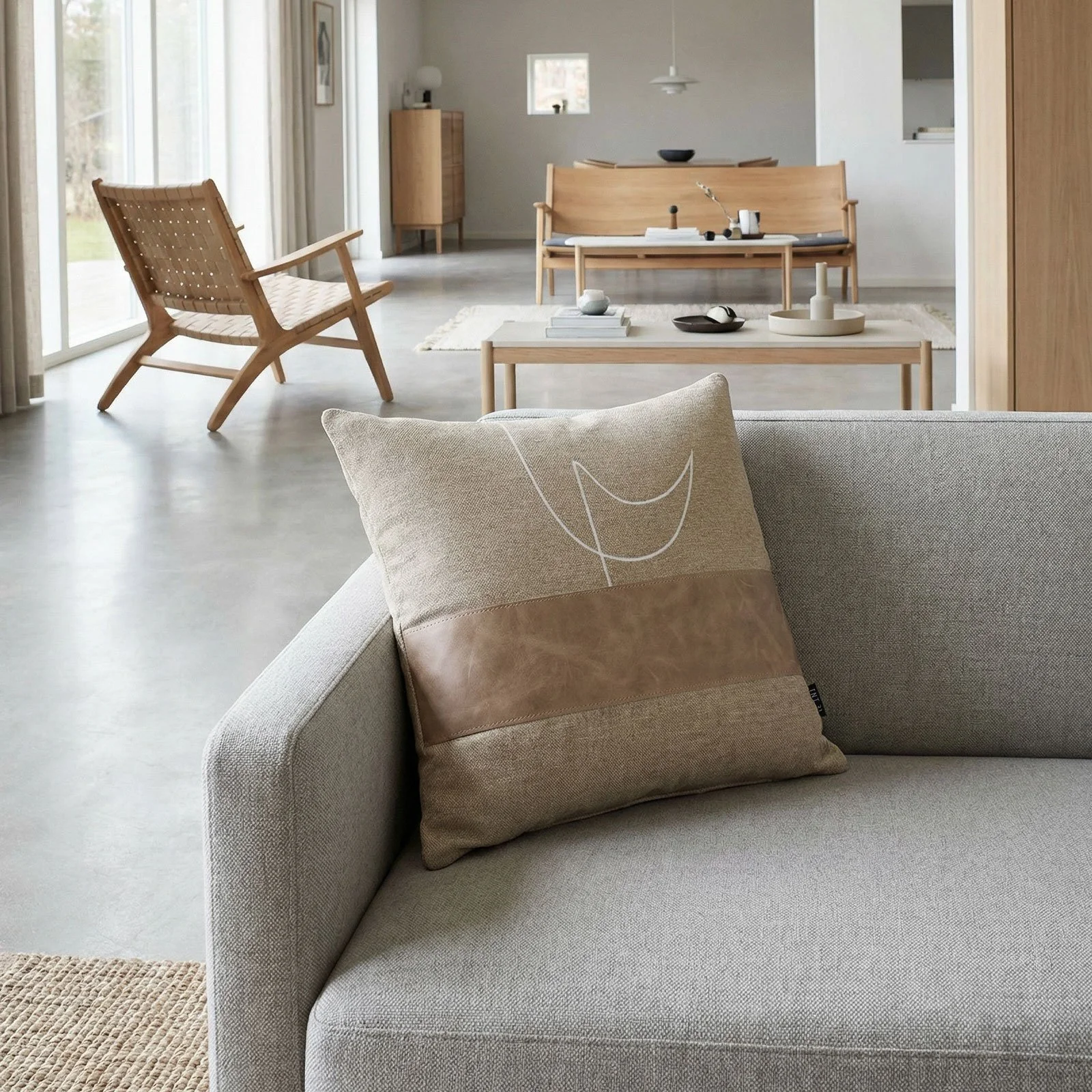 RAIO_02 decorative cushion in beige textile with tan leather panel and abstract white embroidered line detail