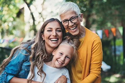 Four people smiling and hugging outdoors with colorful bunting in the background.