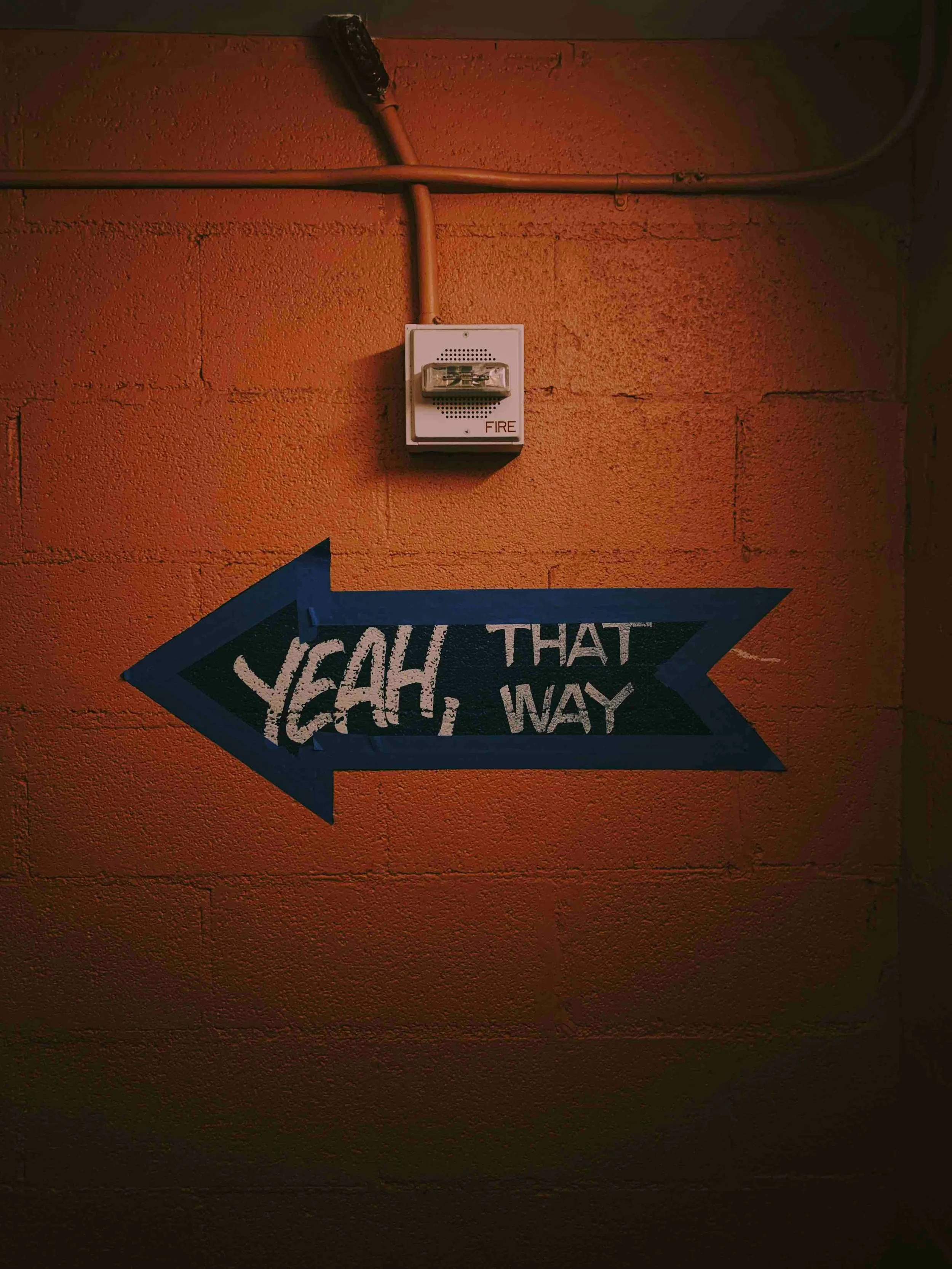Blue arrow sign on an orange brick wall with the text 'Yeah, that way' pointing to the left.