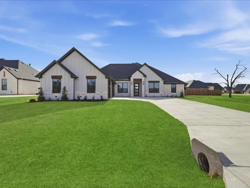 Front view of a modern house with a brick and siding exterior, a driveway, and a green lawn under a blue sky.