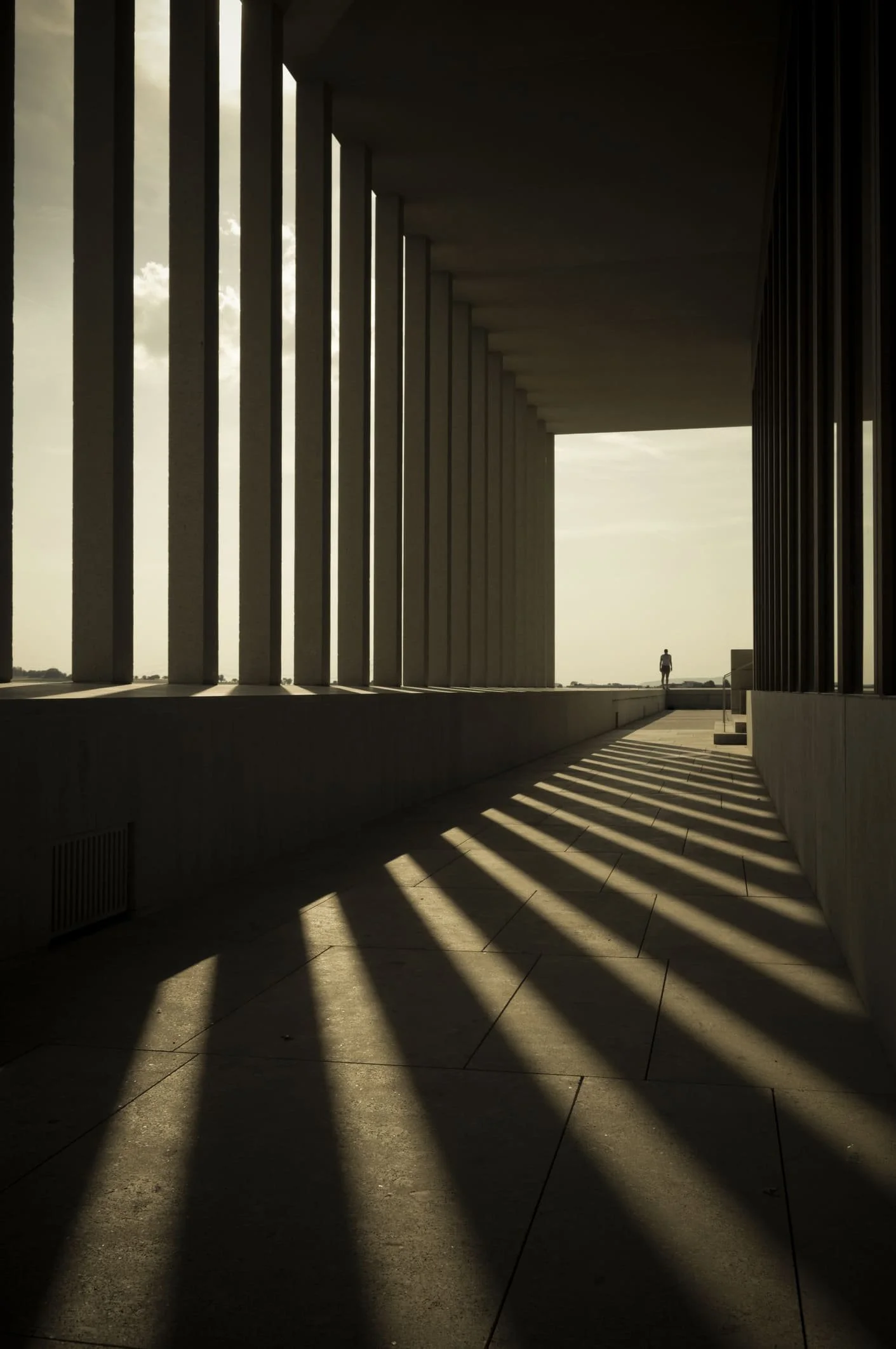 Architektonisches Gebäude mit schrägen Schatten und einer einsamen Person im Hintergrund.