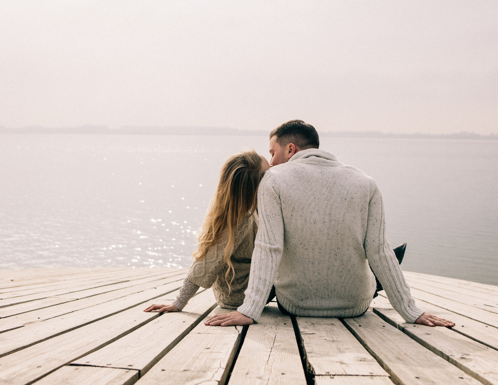 romantic man and woman kissing while sitting on a lakeside dock showing married connection