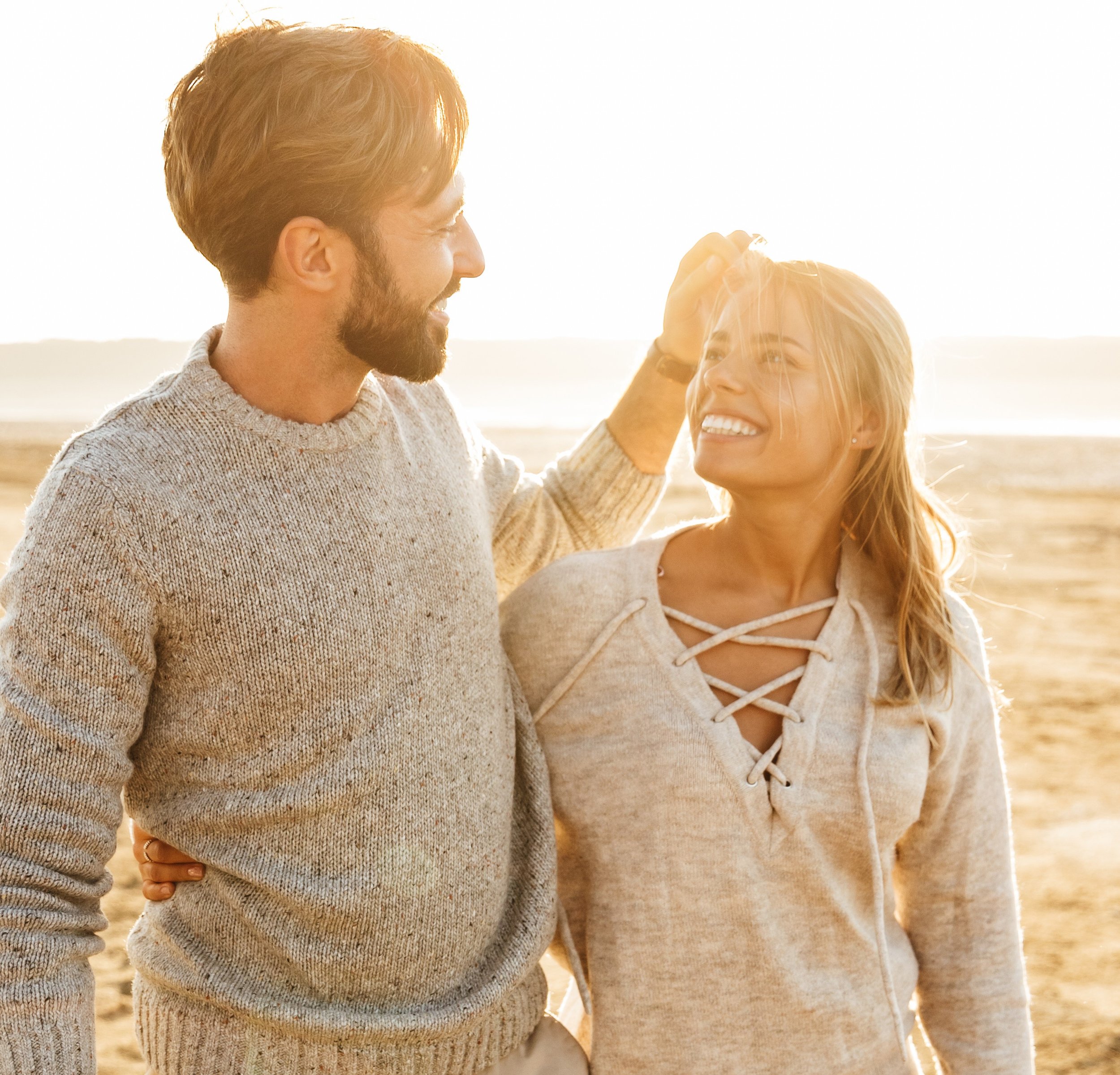 couple smiling together on a beach at sunset, sharing a close, affectionate moment.