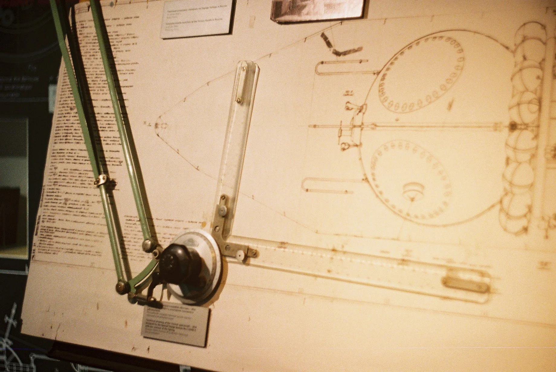 A mechanical device with rods and a circular protractor, placed on a surface with a detailed drawing or schematic, possibly related to engineering or drafting.