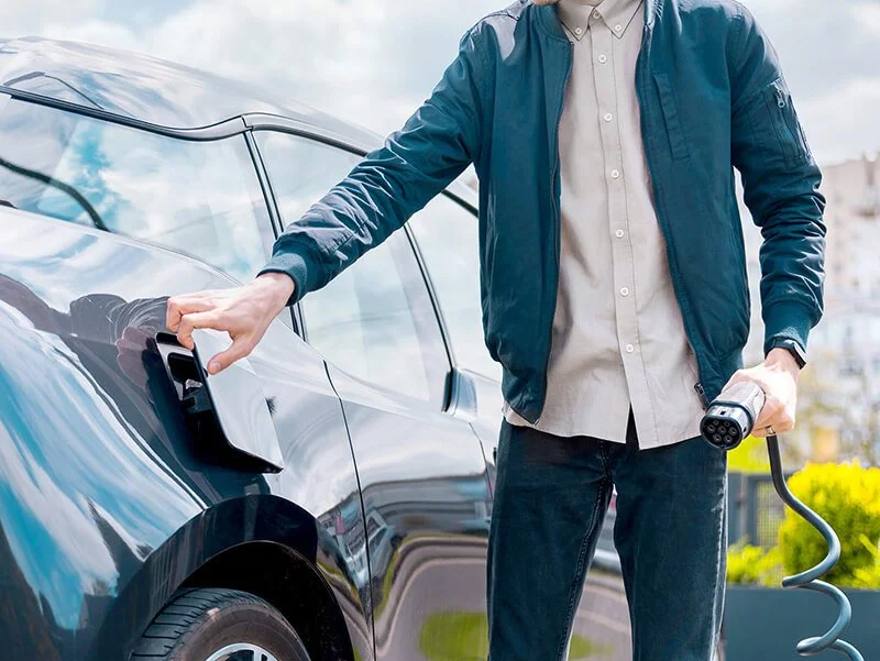 A man opening the charging cap on his EV while holding a Voqa commercial EV charger handle in his other hand
