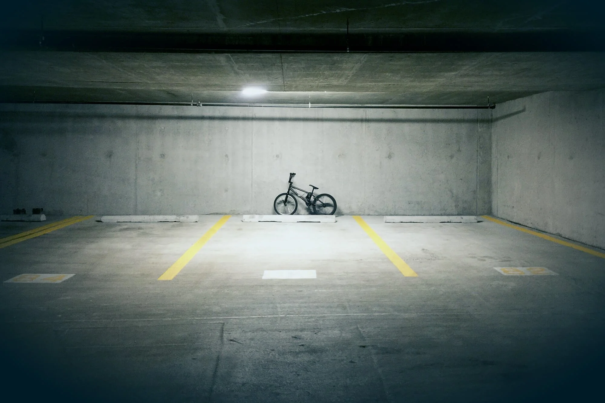 Empty underground parking garage with a single bicycle parked in a designated space against a concrete wall, illuminated by overhead lighting.