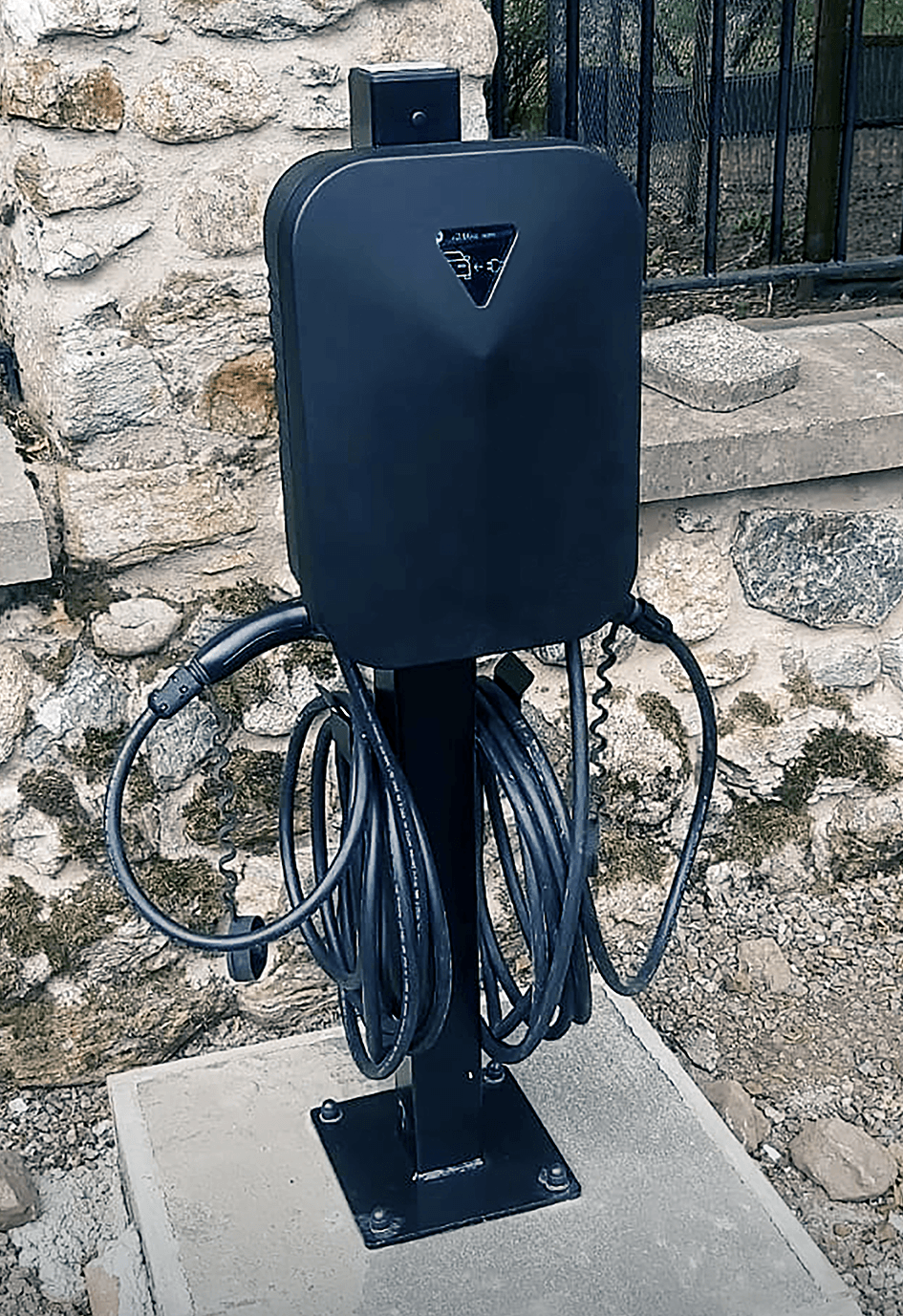 The Voqa One with its dual tethered cables neatly rolled up and fitted to a black pole on a concrete base in front of a stone wall - Installed at Aboyne Loch Caravan Park